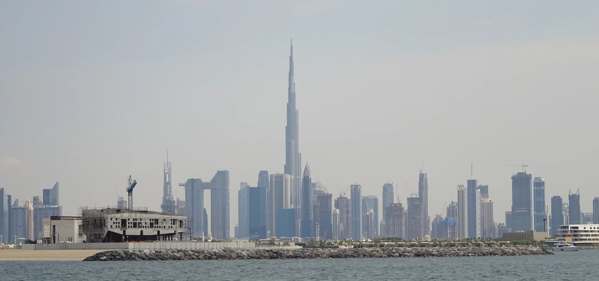 Horizonte de Dubái con el Burj Khalifa sobre las torres, visto a través del mar en calma bajo un cielo pálido