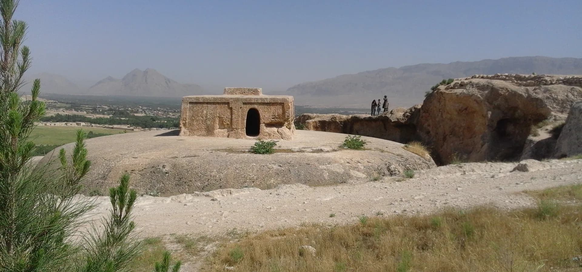 Takht-e Rostam's carved stupa top on a rocky hill above the green Aybak valley, mountains on the horizon