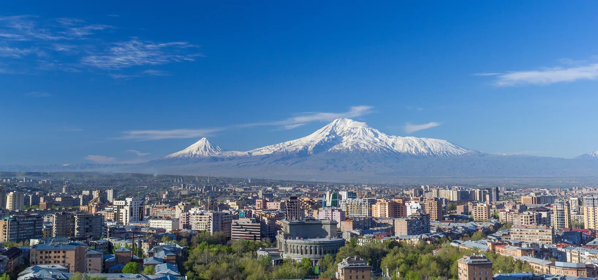 Snow-capped Mount Ararat rising behind the Yerevan skyline and the round Opera house on a clear spring day