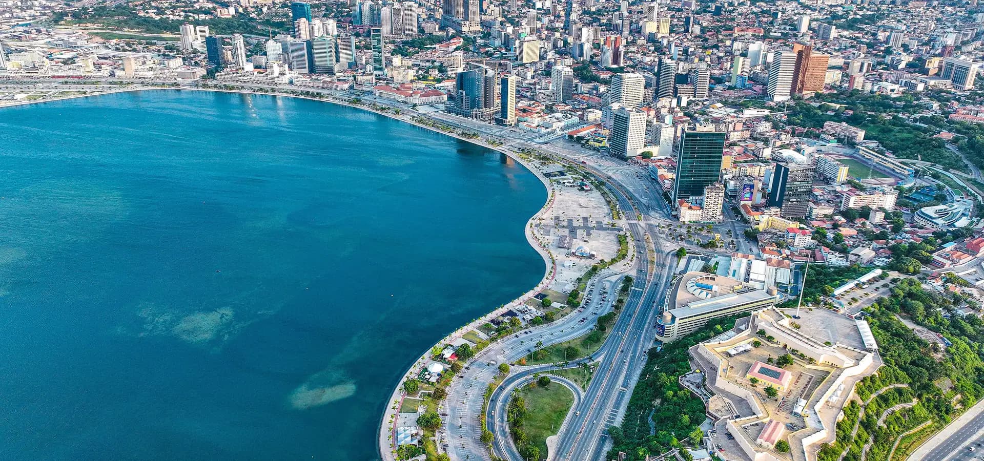 Luftbild der türkisfarbenen Bucht von Luanda, der geschwungenen Promenade Marginal, der sternförmigen Festung und der Skyline