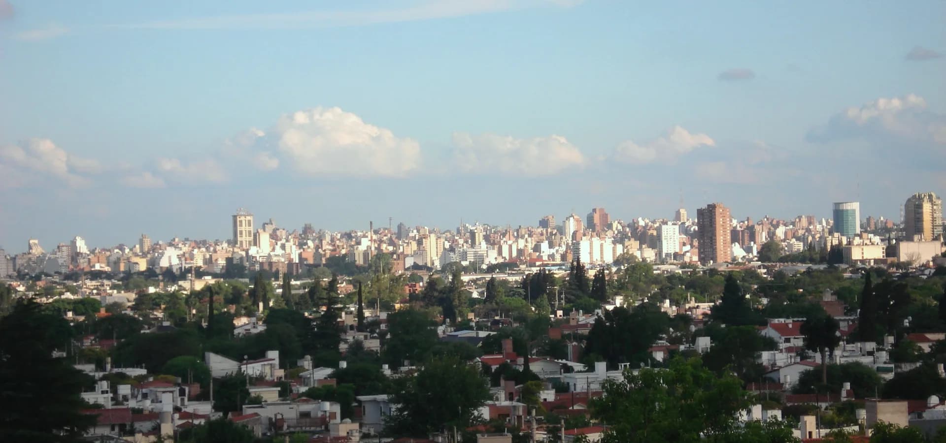 Panorámica de Córdoba, Argentina, con torres altas en el horizonte tras barrios verdes y arbolados