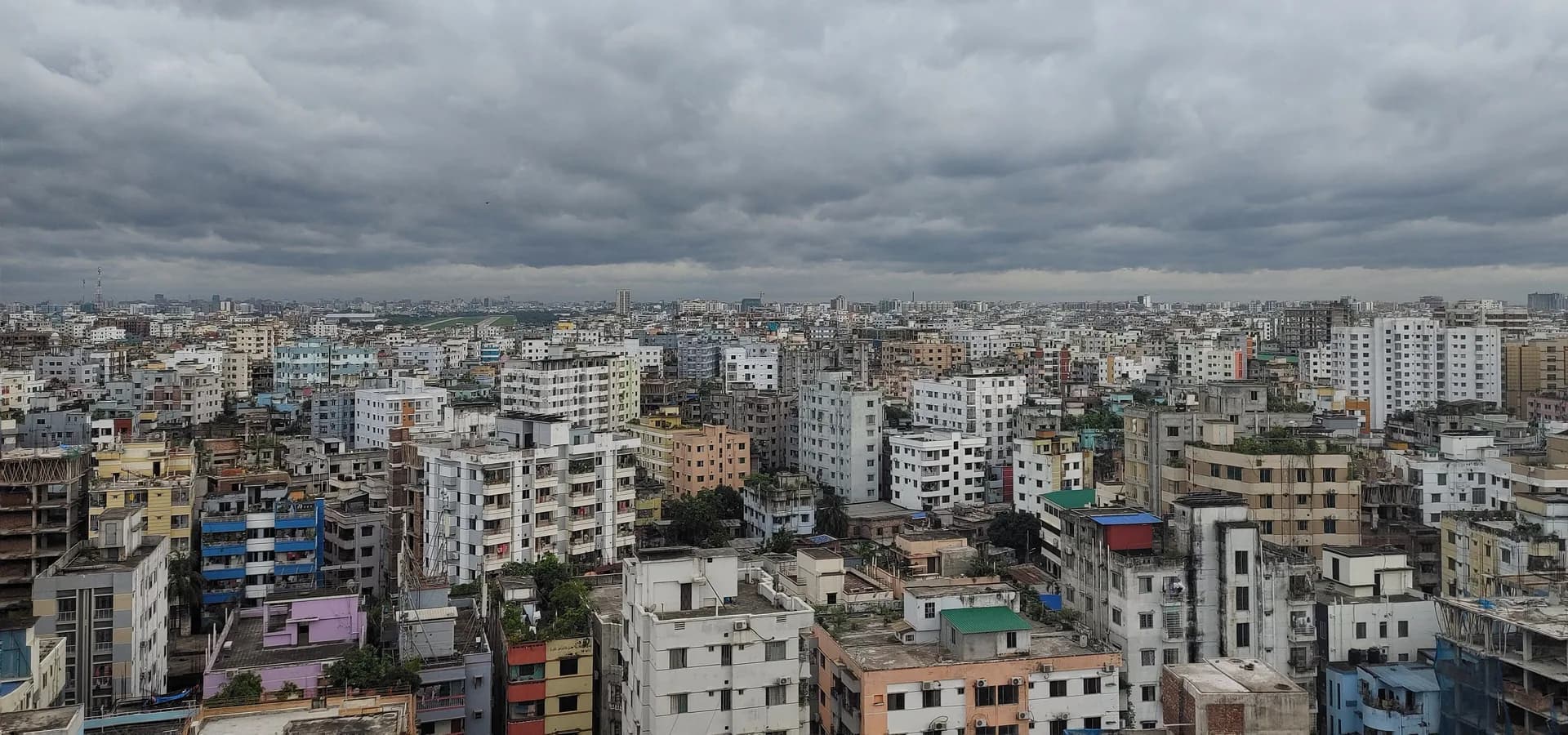 Dhaka rooftops and apartment blocks stretching to the horizon under a wide sky of gray monsoon clouds