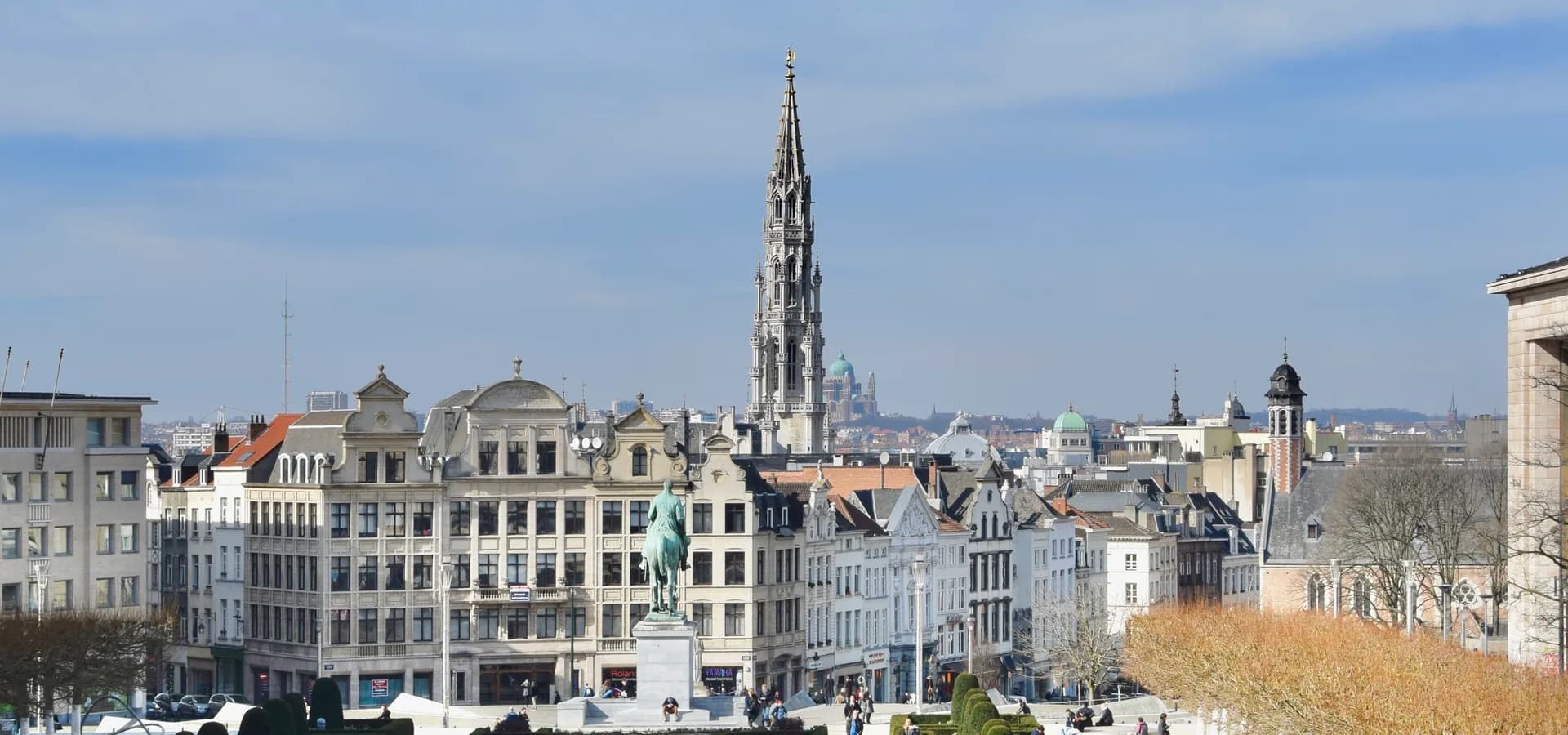 Jardines formales del Mont des Arts que conducen a tejados antiguos y a la aguja del Ayuntamiento bajo un cielo azul pálido