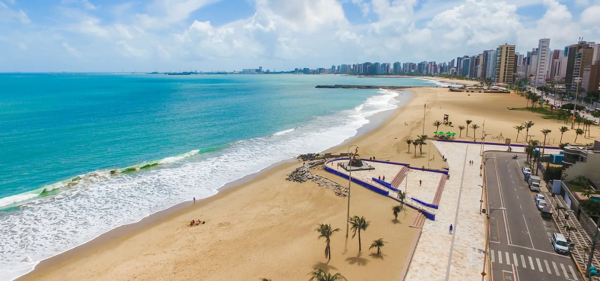 Aerial view of Praia de Iracema, with turquoise sea, golden sand, palm-lined promenade and high-rises along the shore