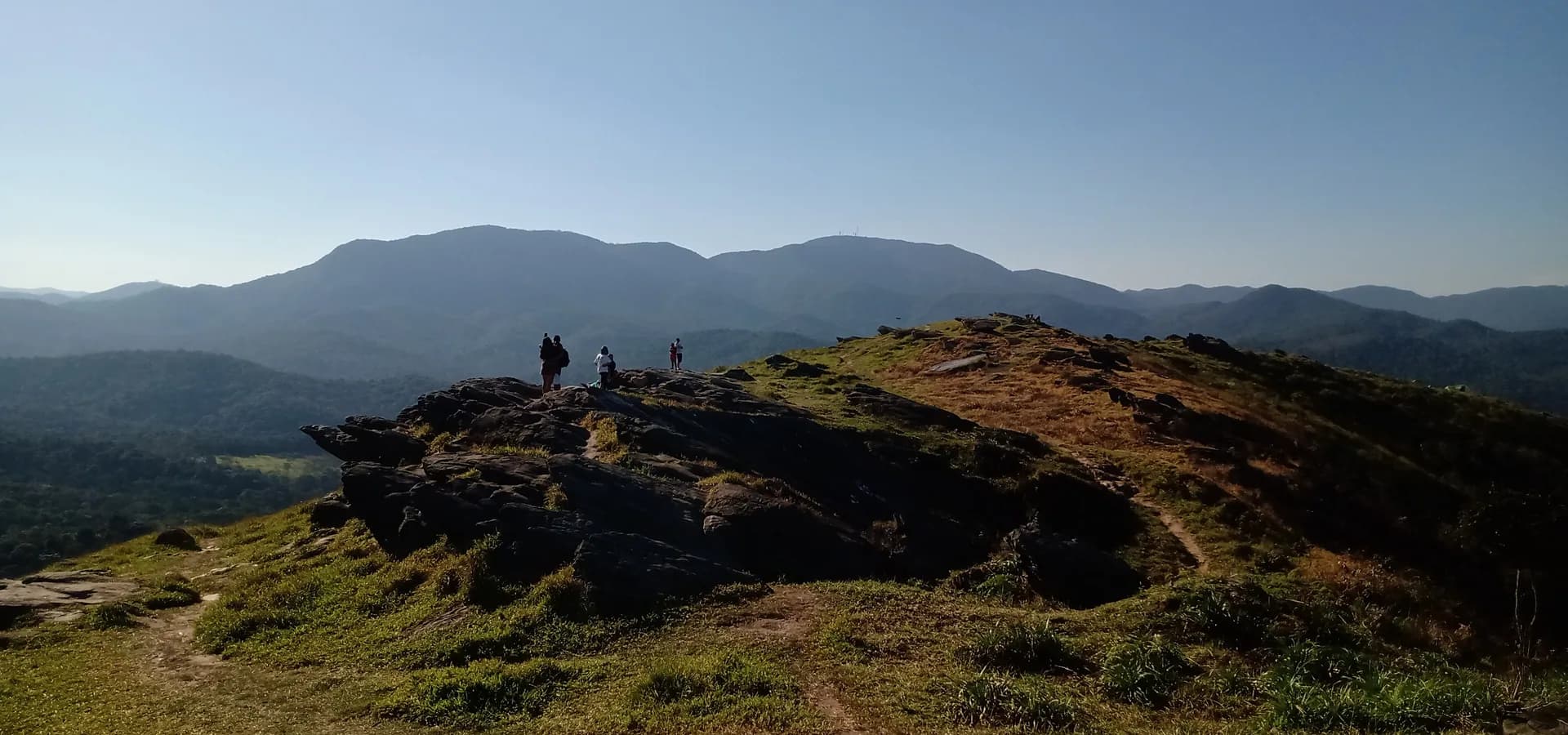 Rocky grassy hilltop in northern Guarulhos facing forested mountain ridges under a clear blue sky