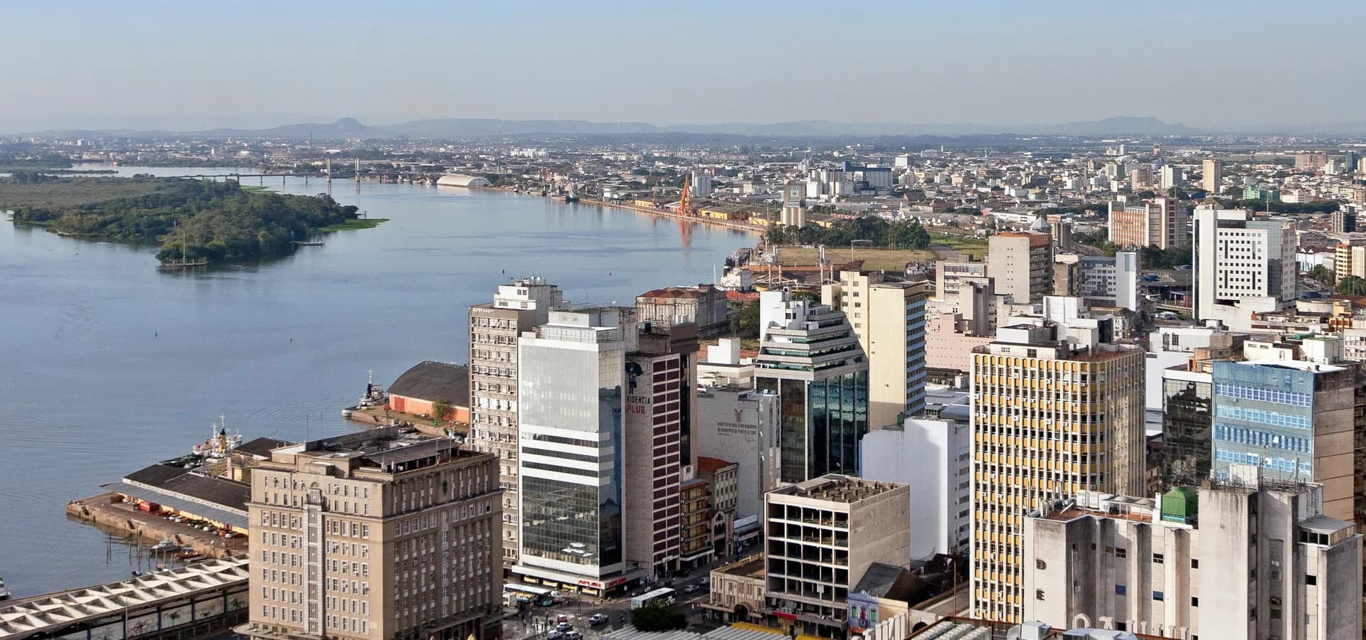 Vista aérea das torres do centro e do porto de Porto Alegre ao longo do largo Guaíba, com ilhas verdes