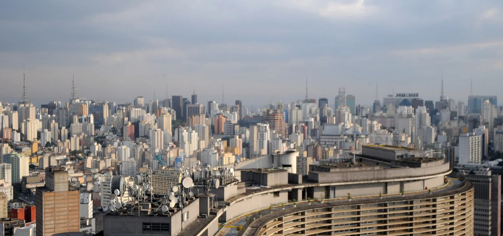 Densa silueta urbana de São Paulo bajo un suave cielo nublado, con el ondulado edificio Copan curvándose en primer plano