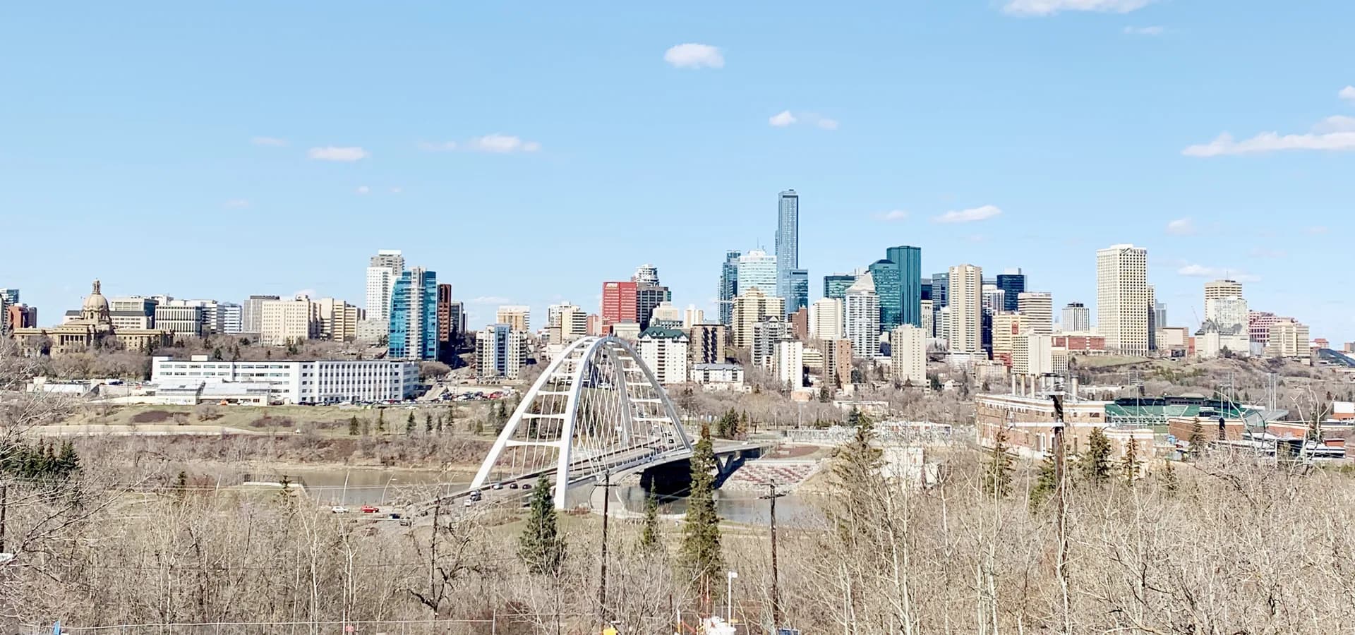 Skyline do centro de Edmonton sobre o vale do rio, com o arco branco da Walterdale Bridge e a cúpula do Legislativo