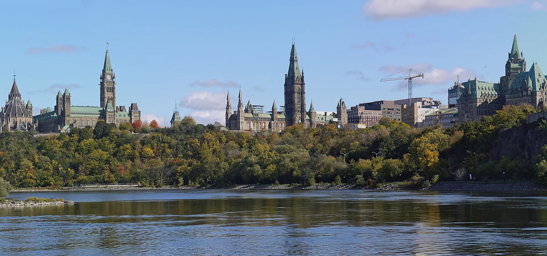 Parliament Hill towers and the Château Laurier above autumn trees and the calm Ottawa River