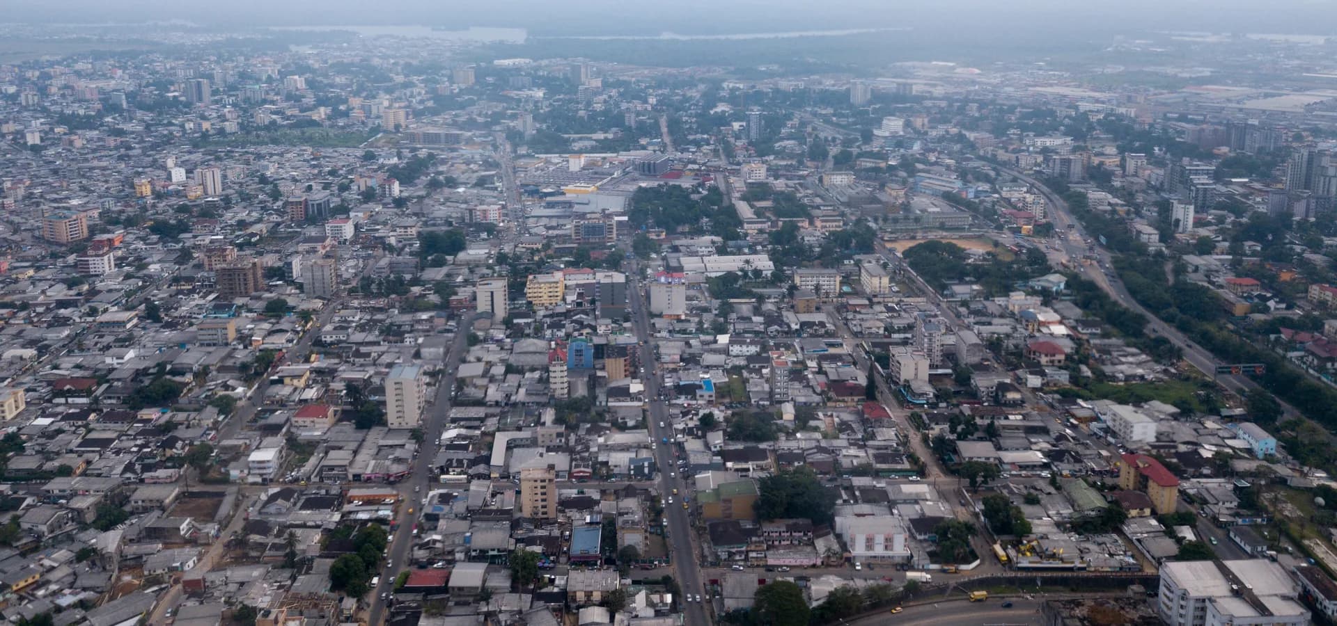 Aerial view of Douala, low rooftops and boulevards stretching toward the Wouri estuary under a hazy sky