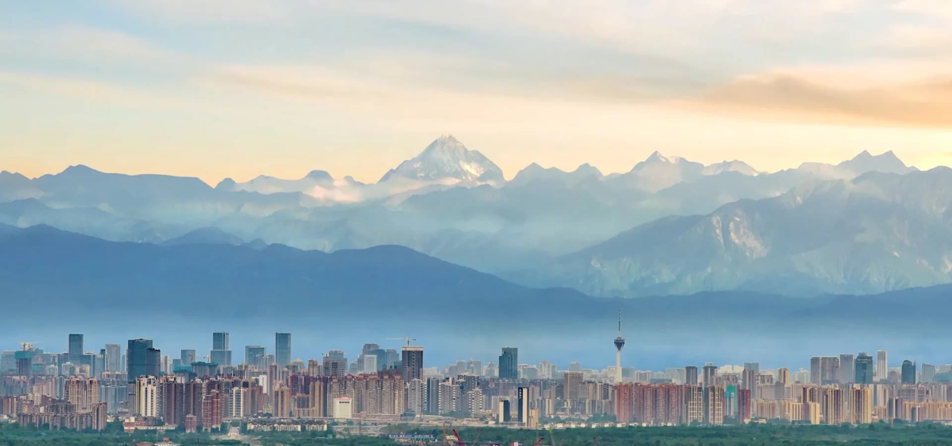 Horizonte de Chengdu con su torre de televisión bajo una hilera de picos nevados que brillan en un suave atardecer