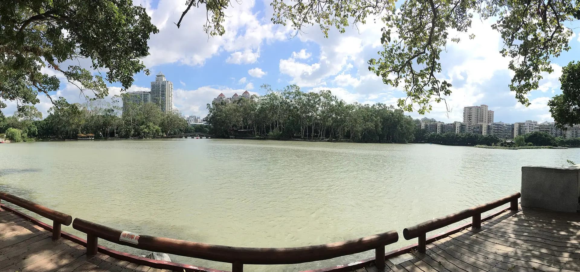 Panorama des Westsees von Fuzhou, von Bäumen gerahmt, mit Steinbogenbrücke, bewaldeten Inseln und Türmen im Hintergrund