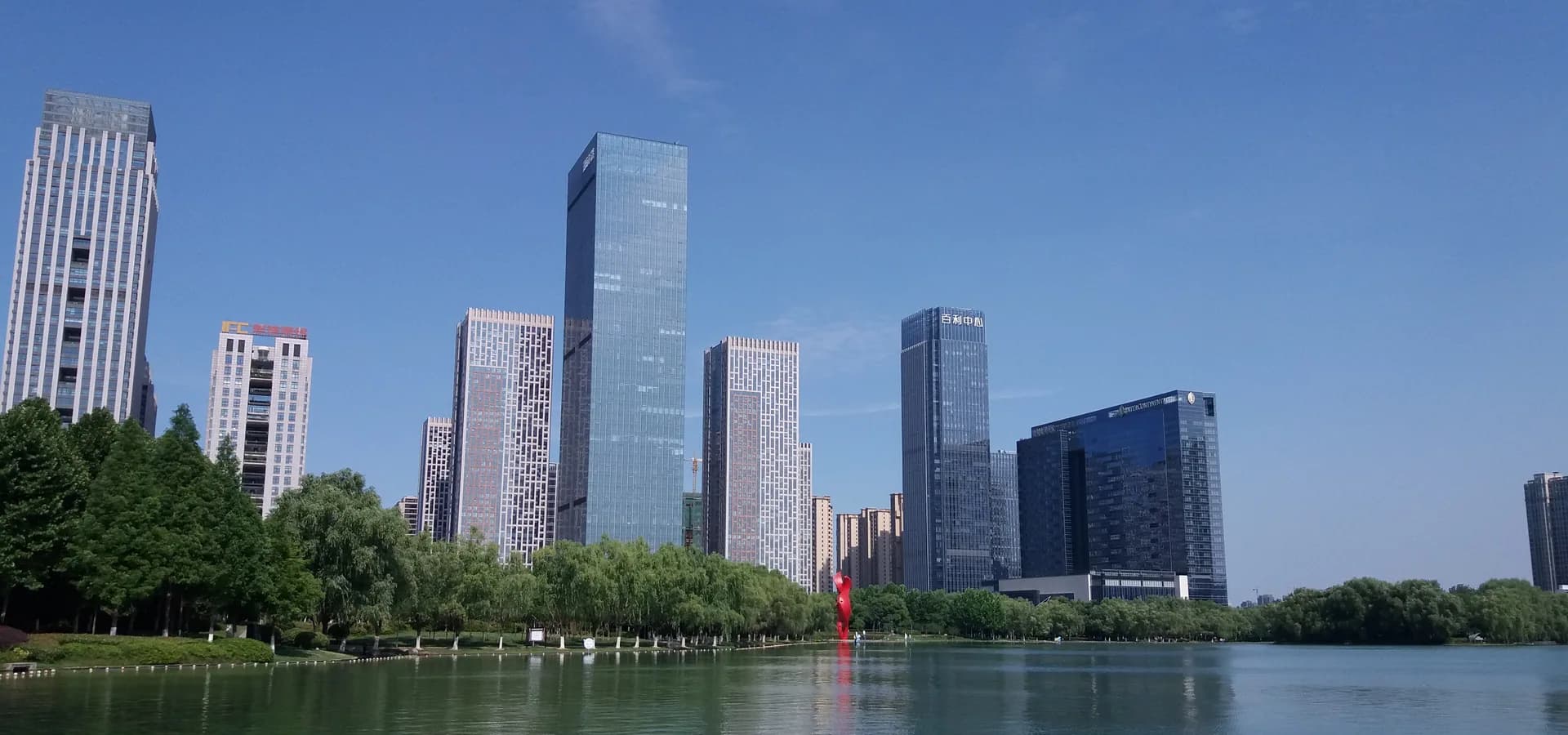 Glass towers rising above willow trees on the shore of Swan Lake in Hefei under a clear blue sky