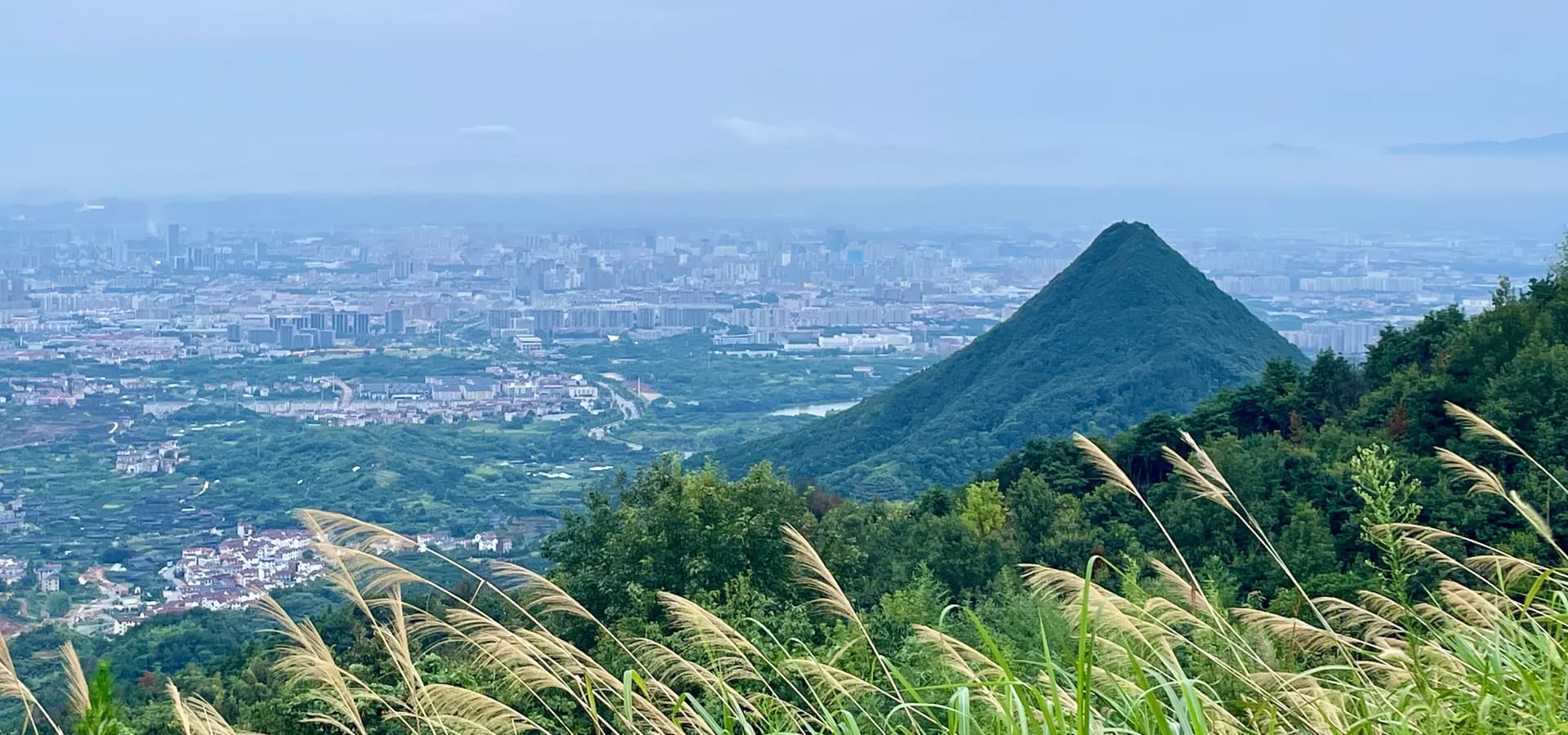 Vista das colinas ao norte de Jinhua sobre campos verdes e torres da cidade, com o monte Jianfeng em forma de cone
