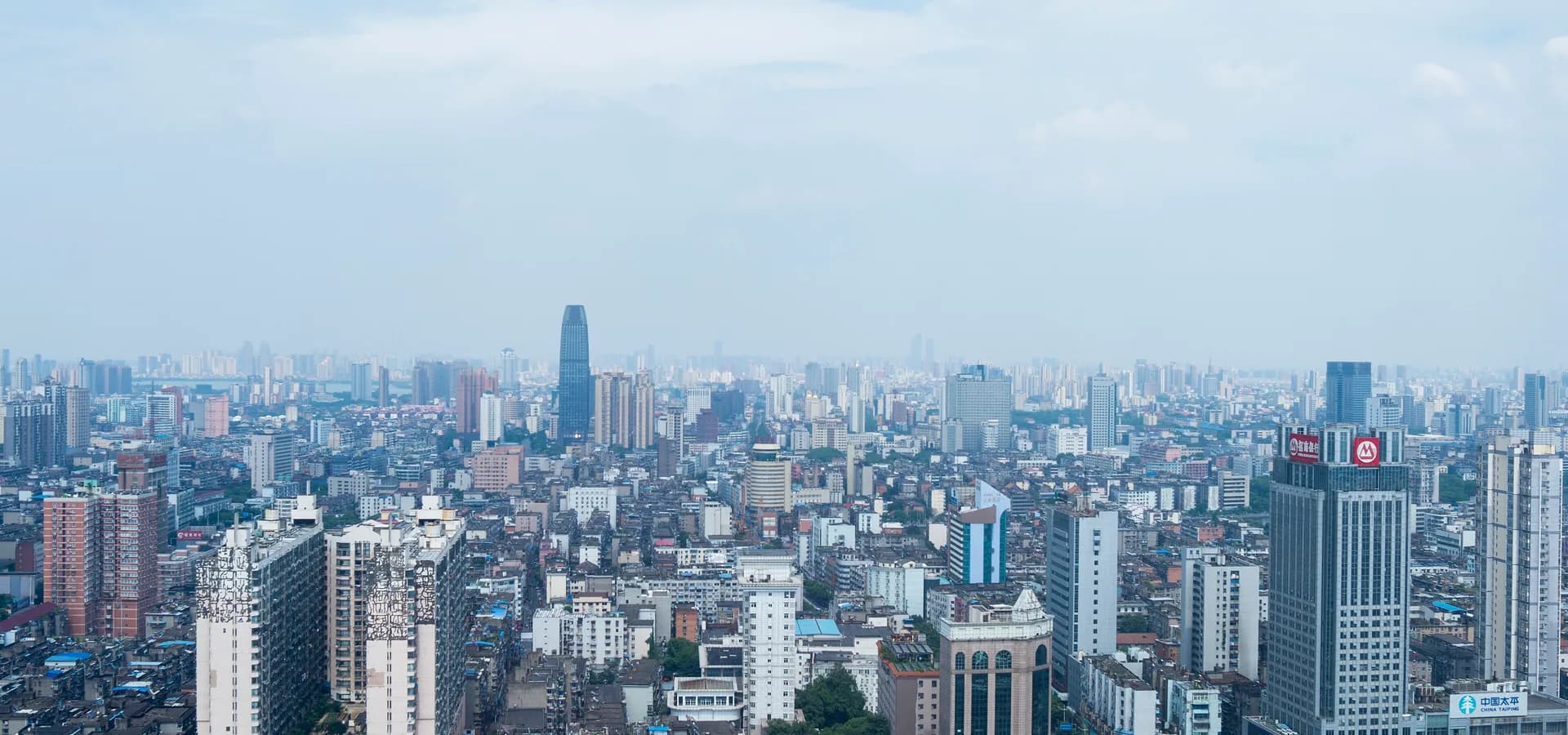 Vista diurna ampla do centro de Nanchang, com fileiras de prédios e torres se estendendo até um horizonte enevoado