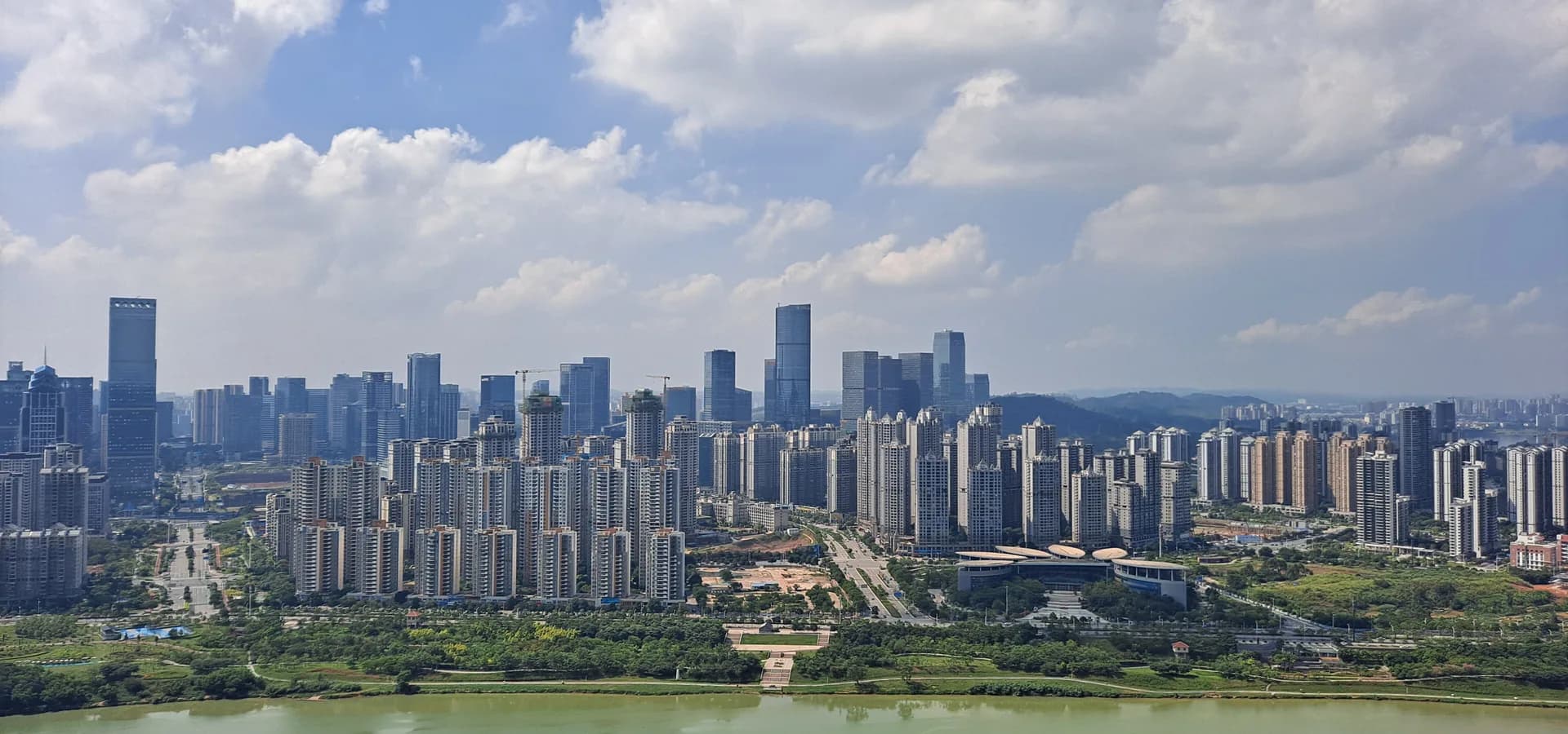 Nanning's high-rises lining the far bank of the green Yongjiang River under a bright sky full of clouds