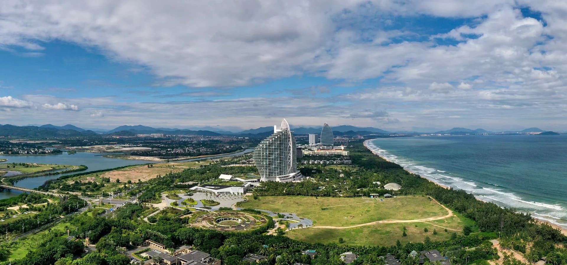 Vista aérea da Baía de Haitang, em Sanya, com lagoas, parques verdes, torres de resorts e uma longa praia em curva