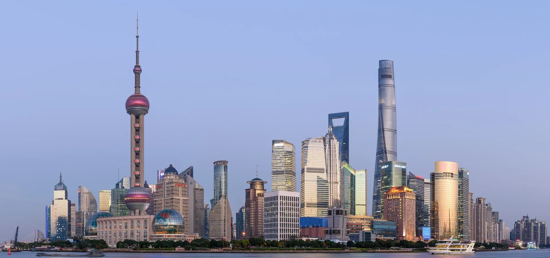 La Torre de la Perla Oriental, la Torre de Shanghái y los rascacielos de Lujiazui al otro lado del tranquilo río Huangpu bajo un suave cielo azul de atardecer