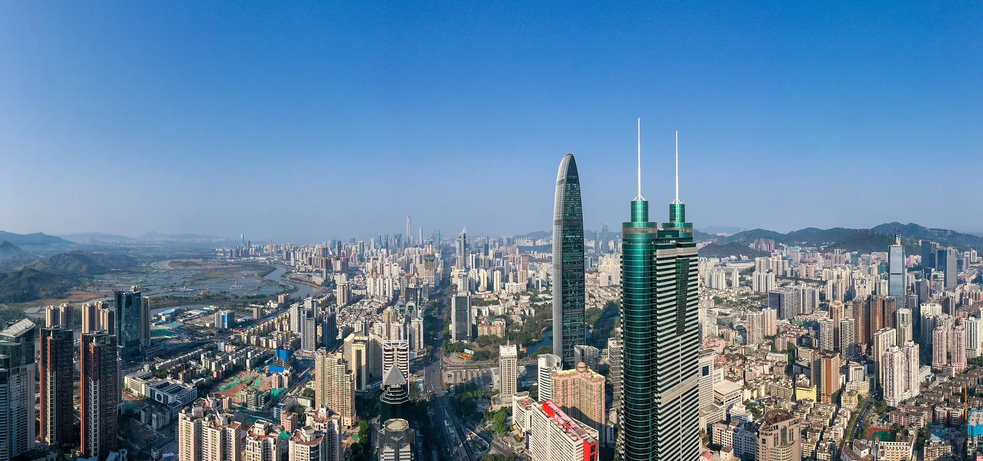 Panorámica aérea de rascacielos de Shenzhen que se extienden hacia colinas verdes bajo un cielo azul despejado