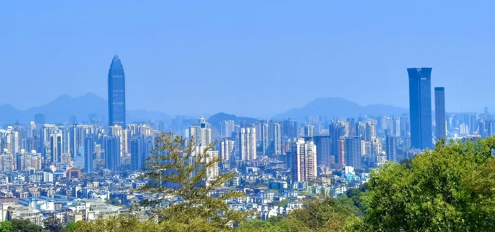 Panorama de las torres de Wenzhou bajo un cielo azul despejado, con crestas de montañas brumosas detrás de la ciudad