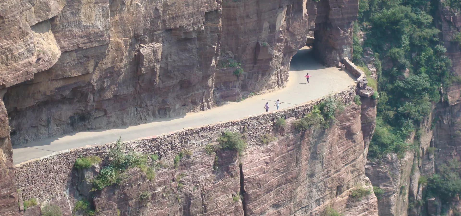 Un camino estrecho tallado en acantilados de arenisca roja en Guoliang, en las montañas Taihang, con diminutos caminantes
