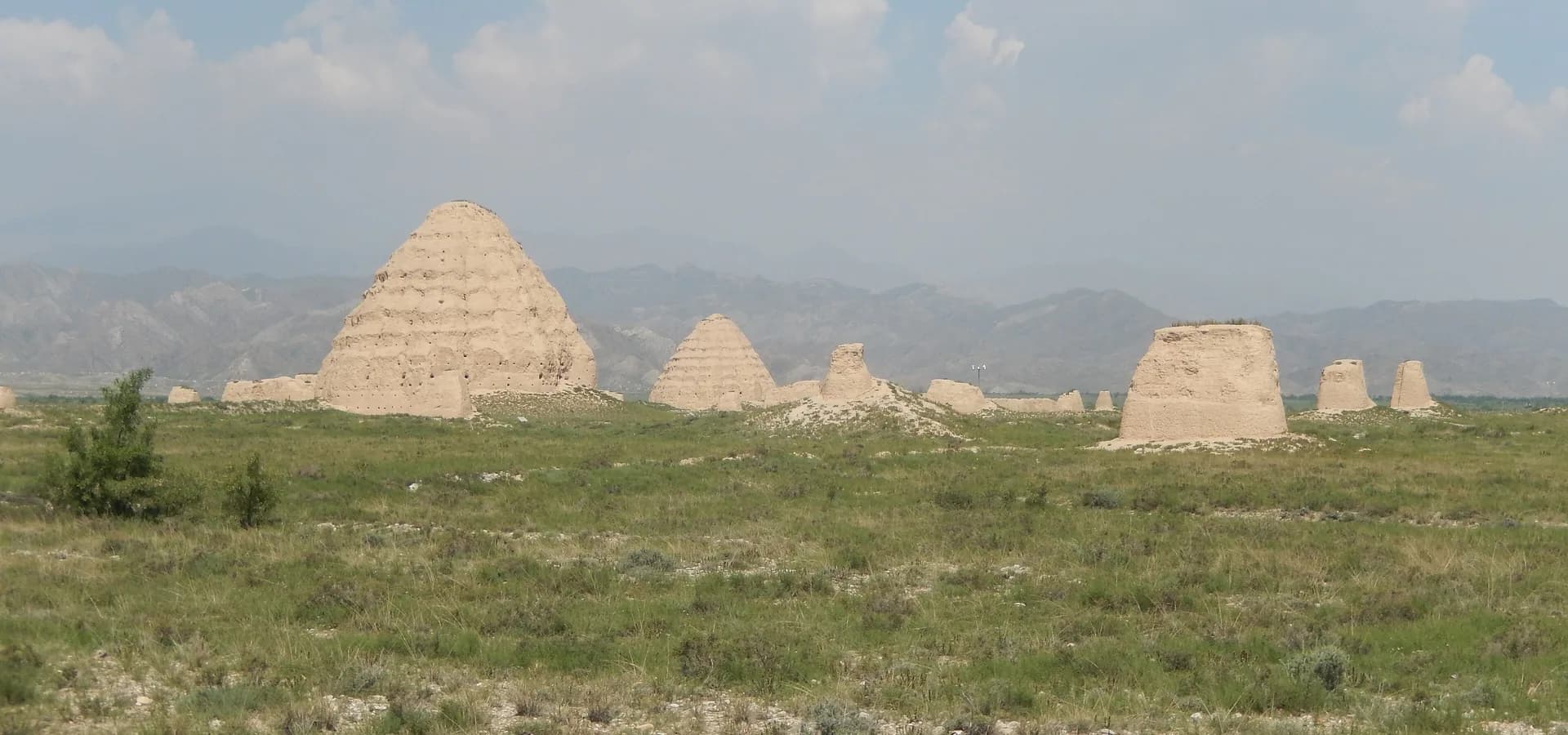Montes de terra dos túmulos imperiais Xia Ocidental na estepe verde sob as Montanhas Helan e nuvens de verão