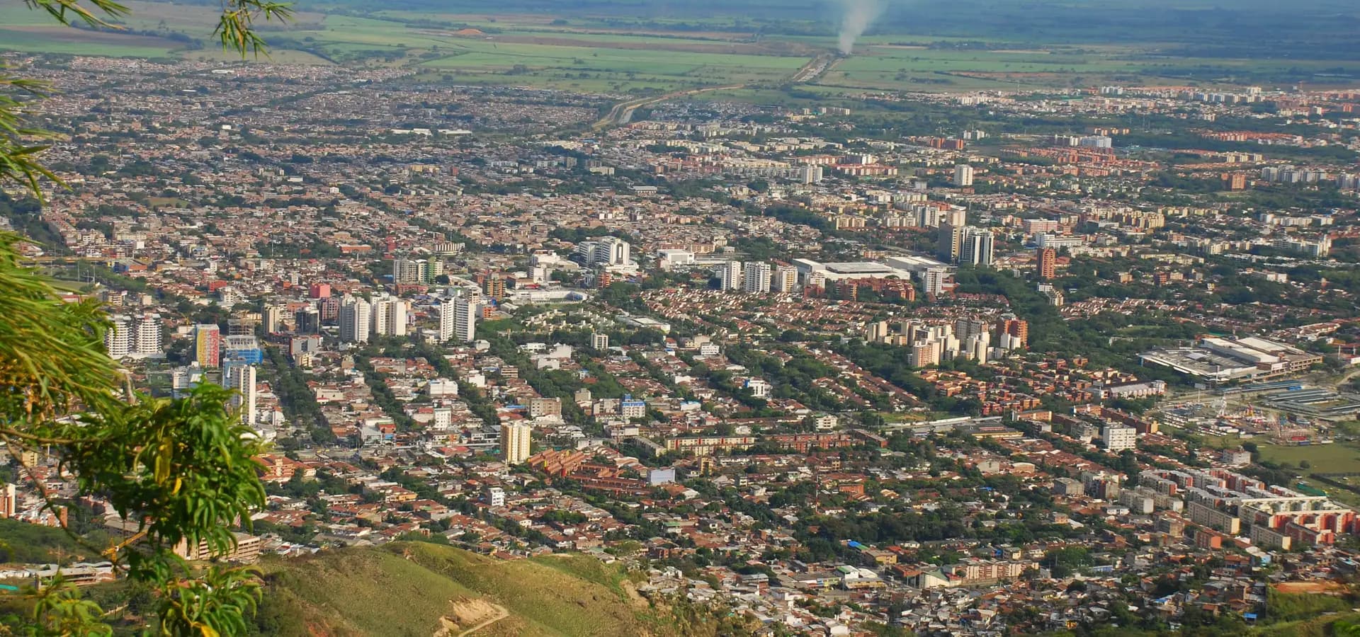 Blick von den grünen Hügeln im Westen über den Süden von Cali, dessen Dächer und Türme sich über das Cauca-Tal ausbreiten
