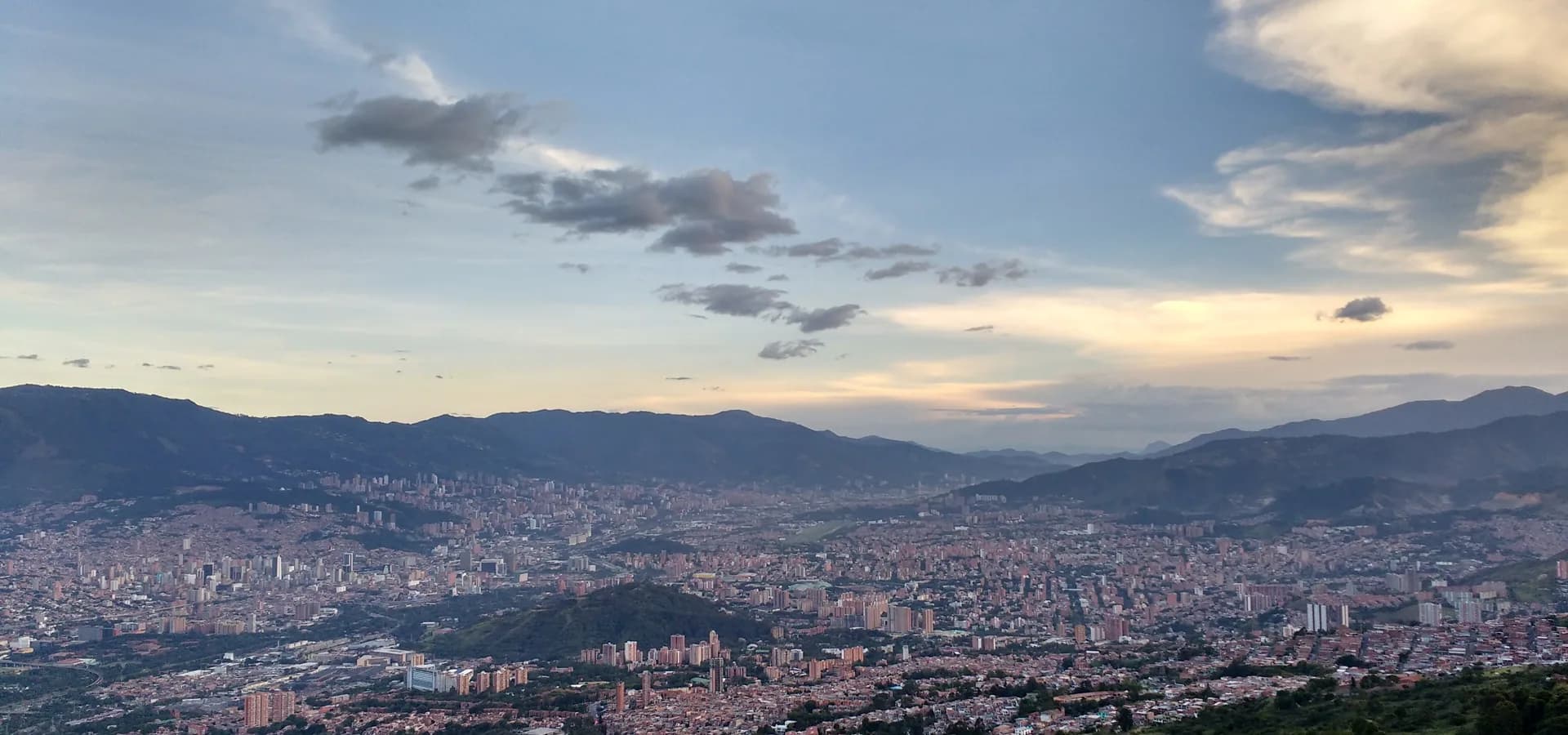 Medellín se espalhando pelo verde Vale de Aburrá ao entardecer, vista do Cerro El Picacho sob um céu amplo.