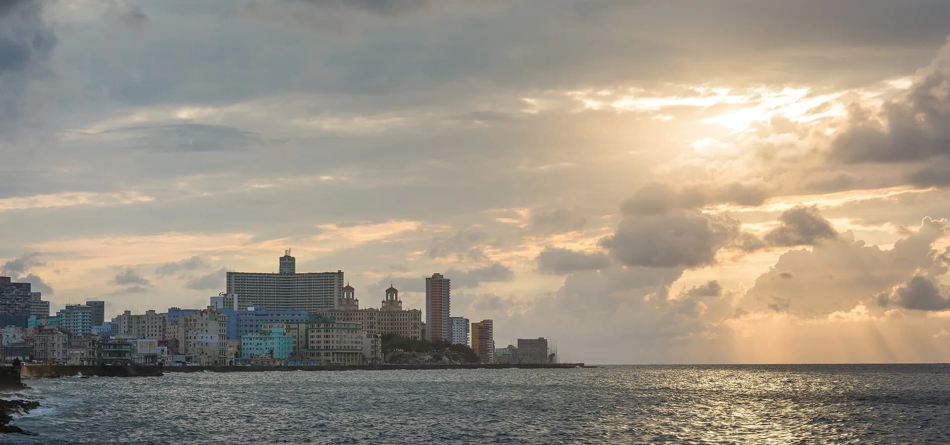 Skyline der Uferpromenade von Havanna entlang des Malecón, die tiefe Sonne bricht durch Wolken über silbernem Meer