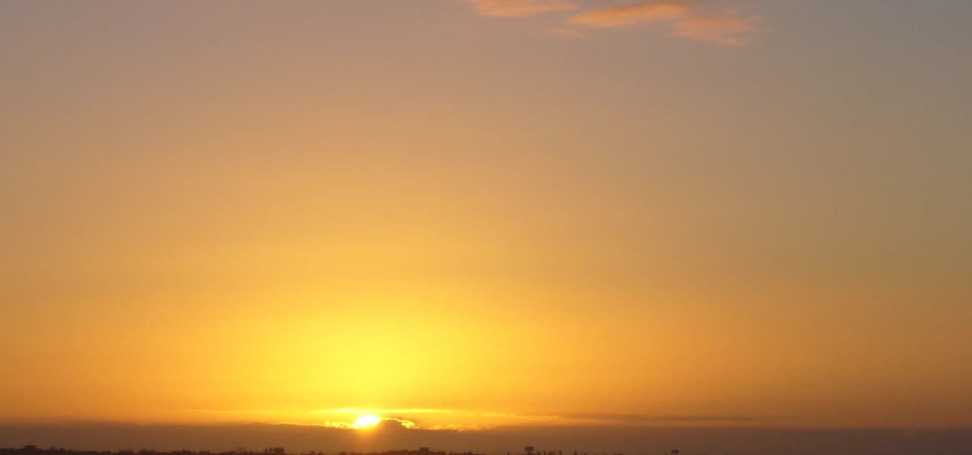 Atardecer dorado sobre la bahía calma de Boca Chica, protegida por un arrecife, con un muelle bajo reflejado en el agua quieta