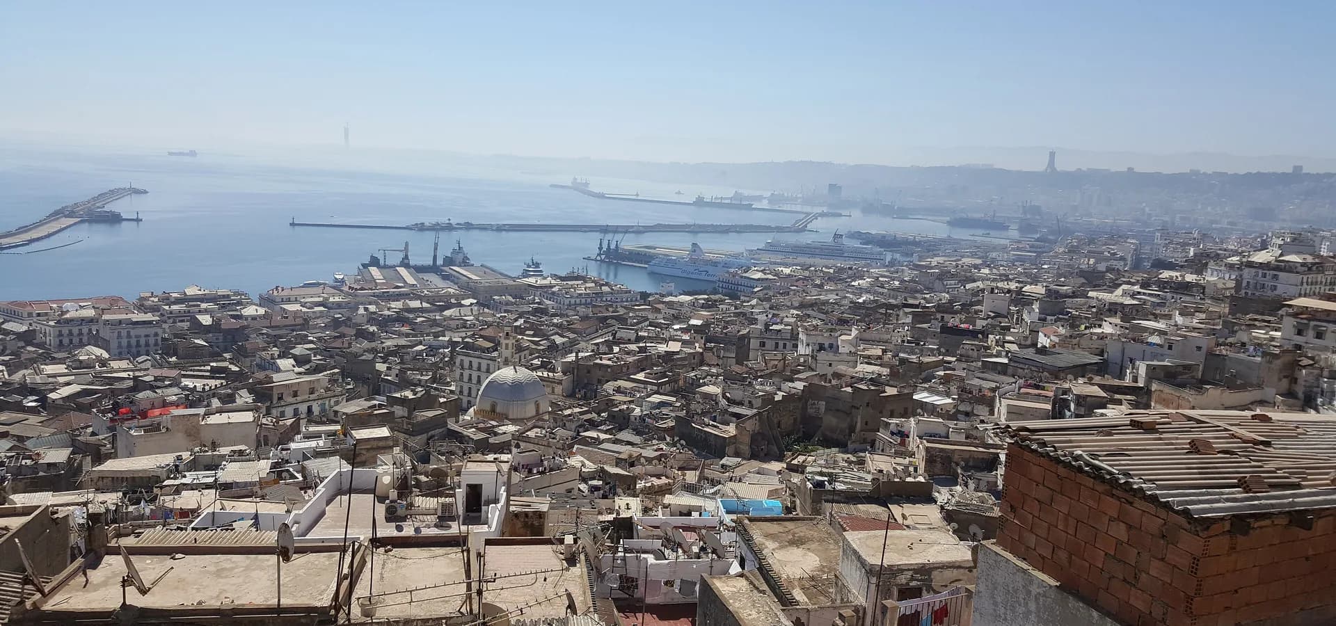 White rooftops of the Casbah of Algiers stepping down the hill toward the harbor and the hazy blue bay