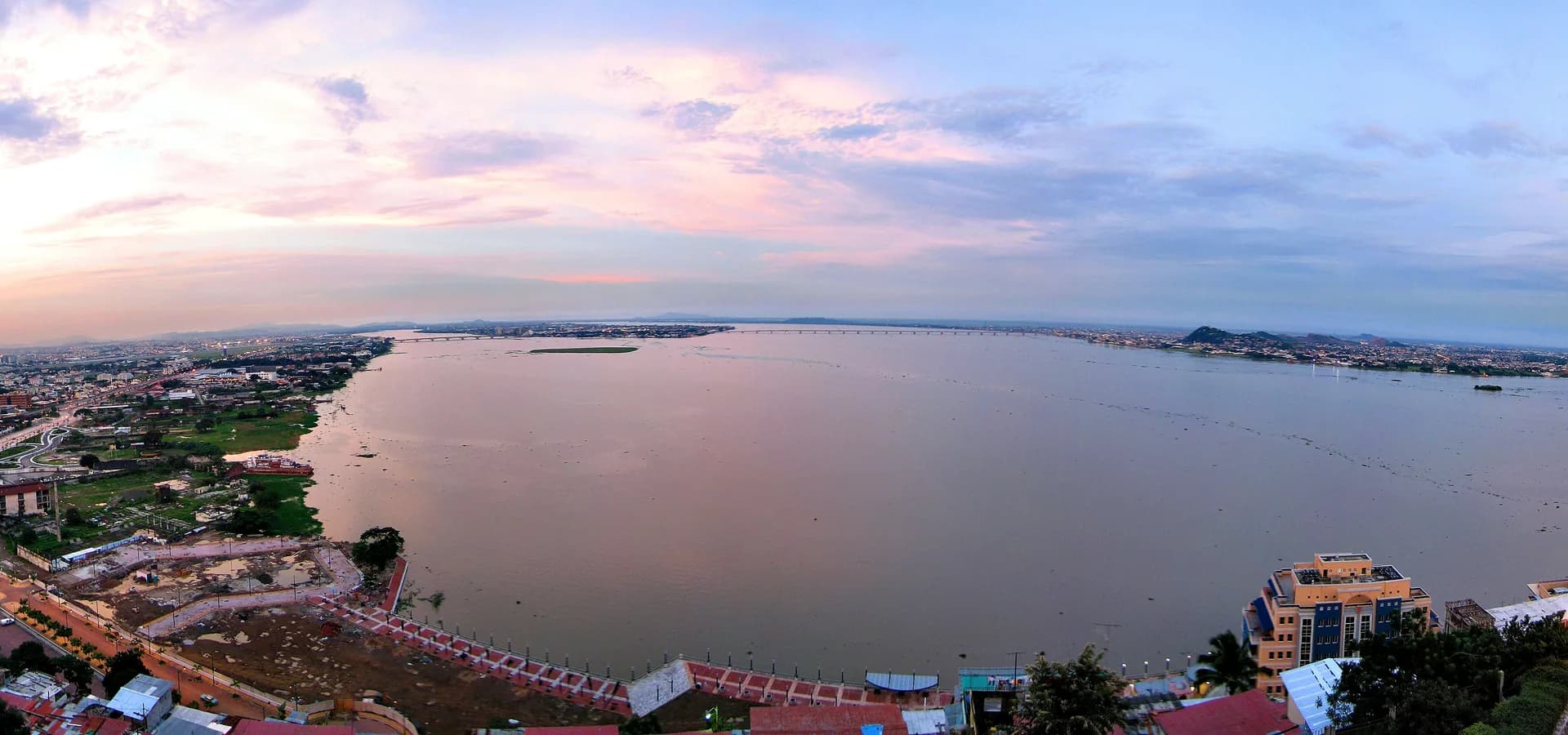 Vista ampla ao entardecer sobre o rio Guayas a partir do Cerro Santa Ana, com Guayaquil se estendendo pela margem sob um céu rosado