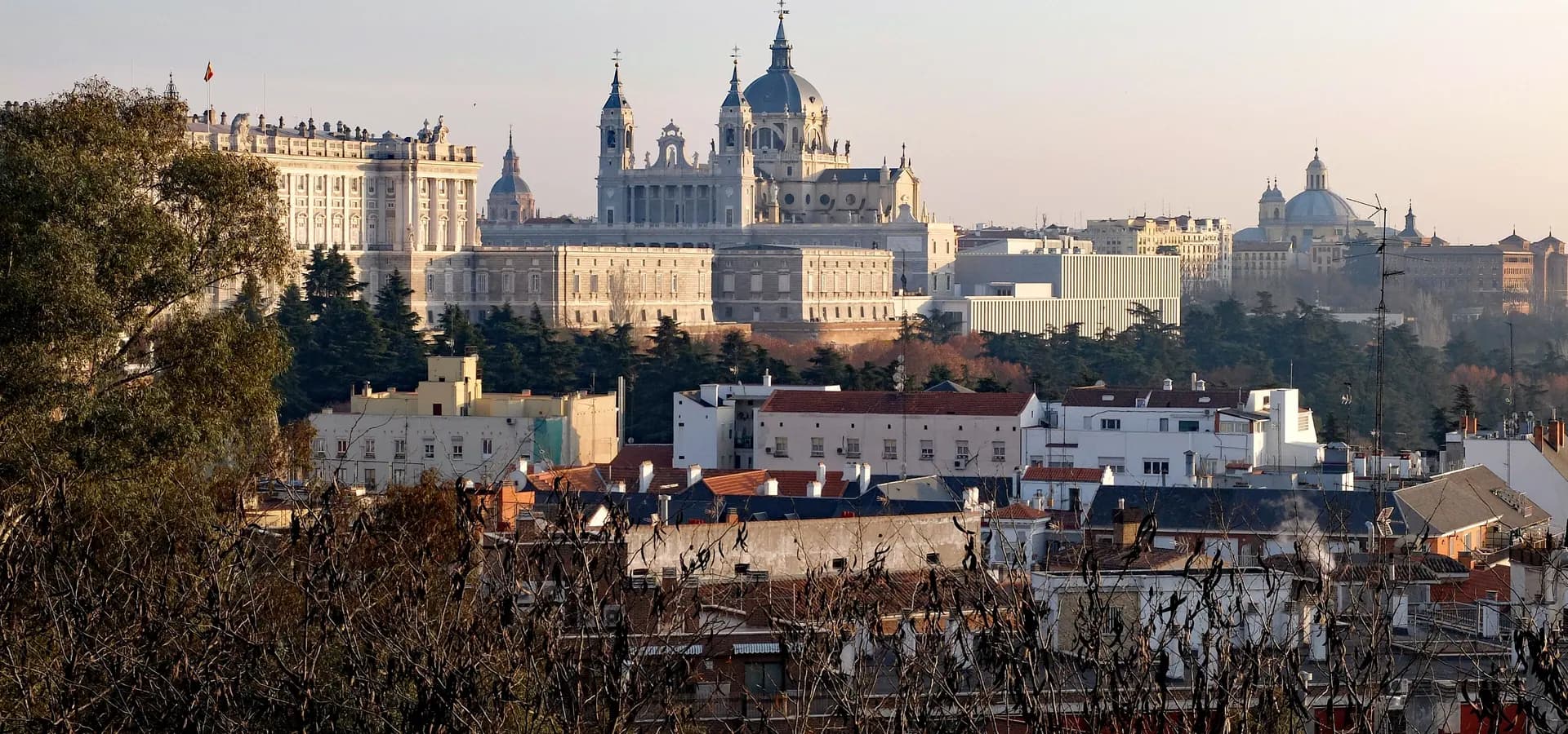 El Palacio Real y la Catedral de la Almudena se alzan sobre los tejados y pinos de Madrid con una cálida luz de atardecer