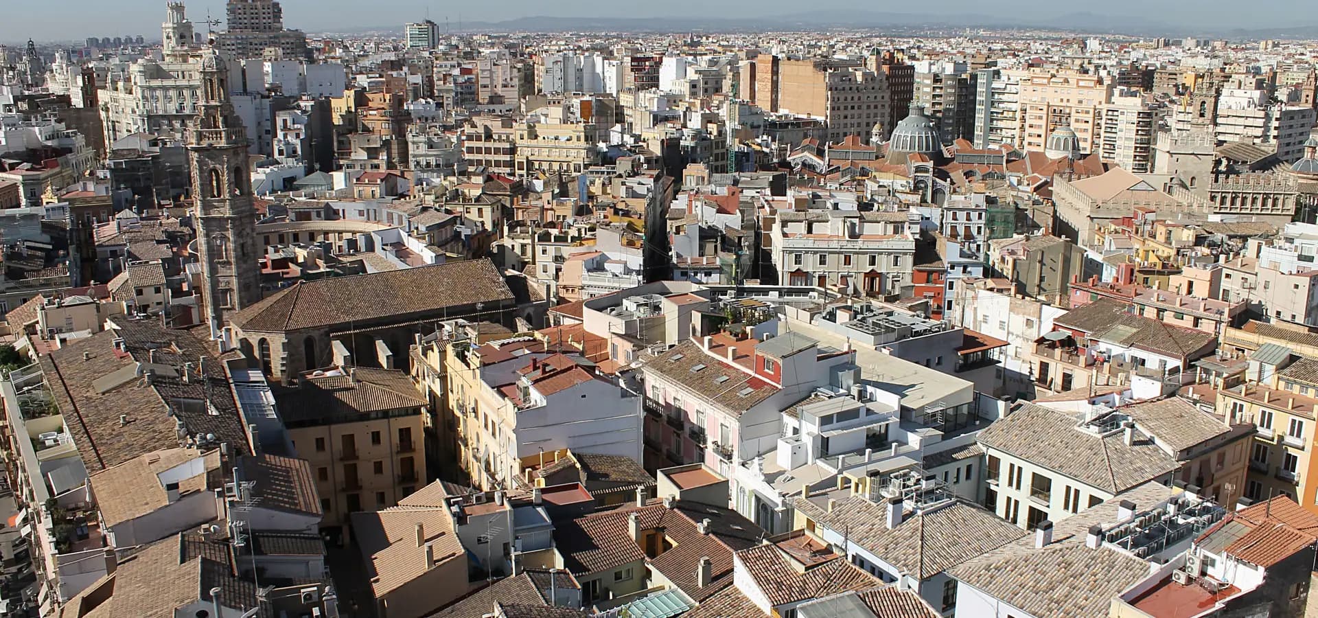 Ziegeldächer der Altstadt von Valencia mit einem barocken Glockenturm und einer Marktkuppel unter klarblauem Himmel
