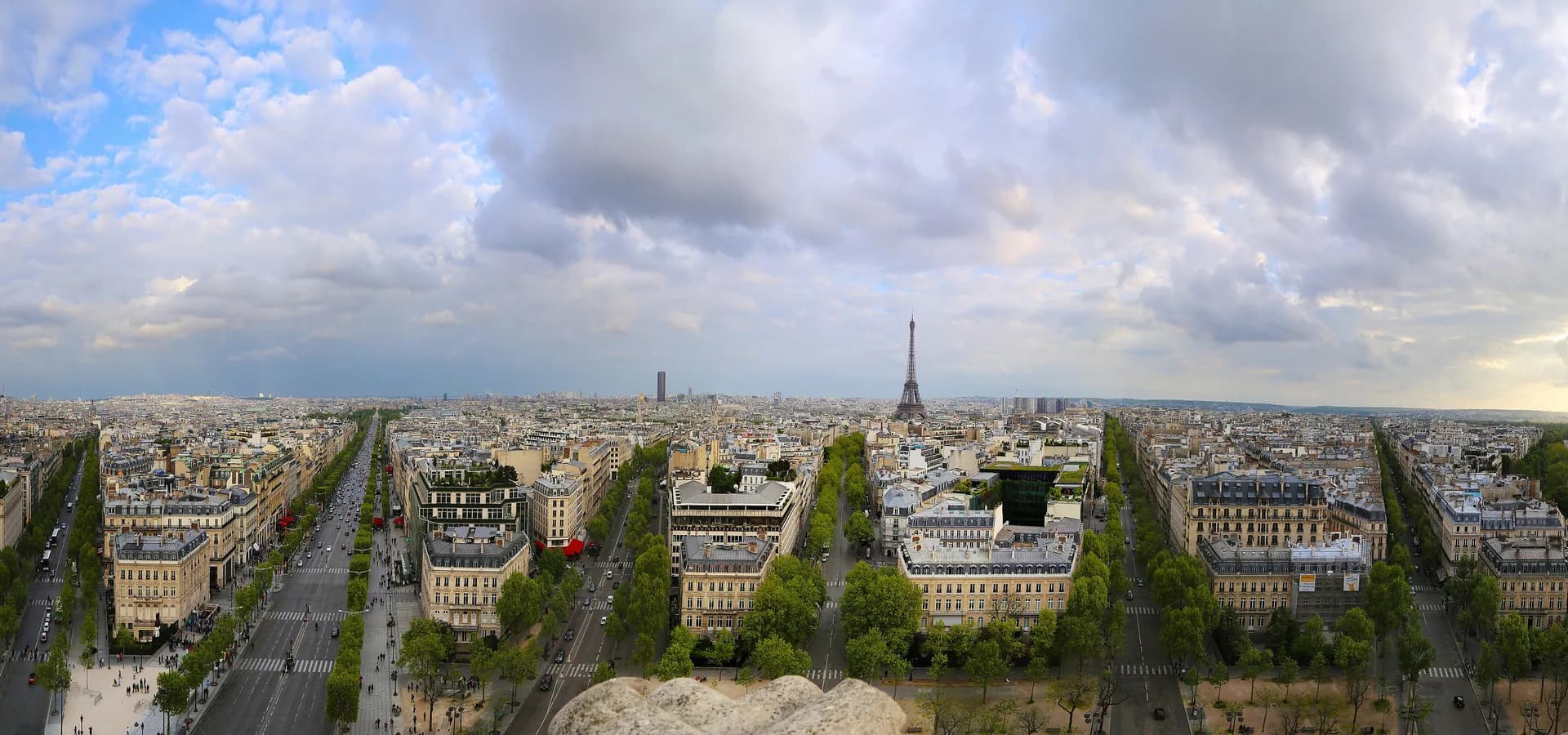 Weiter Blick vom Arc de Triomphe über Haussmann-Alleen und Dächer bis zum Eiffelturm unter Wolken