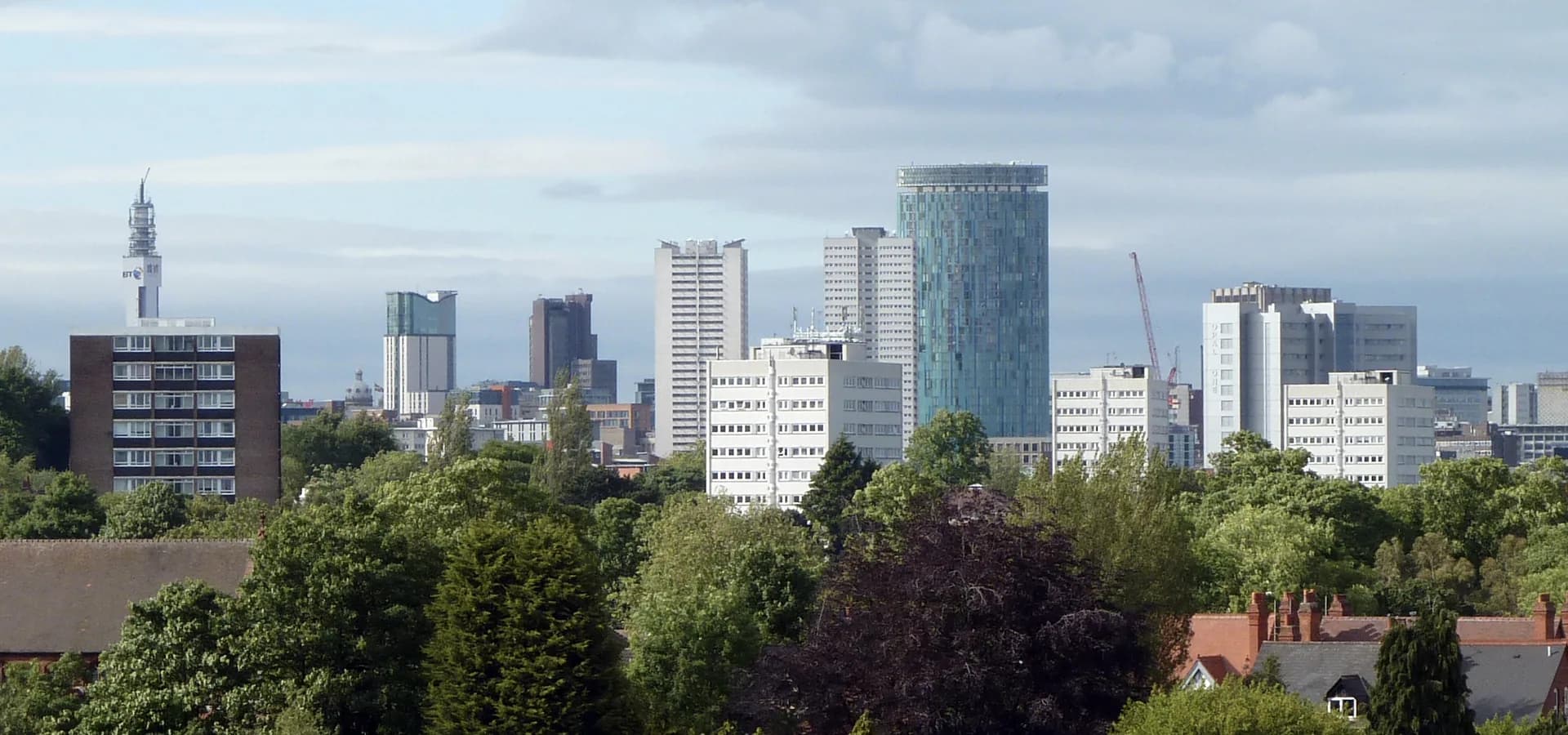 Birmingham skyline of towers, including the round Rotunda and BT Tower, rising above green trees and red roofs in Edgbaston