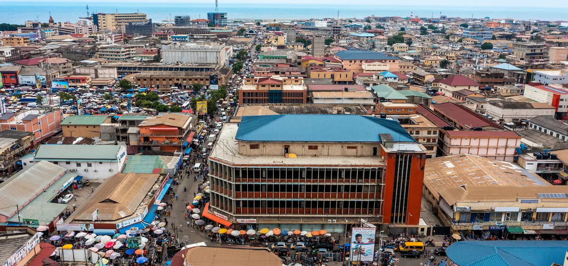 Vista aérea del centro de Acra, con sombrillas de mercado y tejados que bajan hasta el azul golfo de Guinea