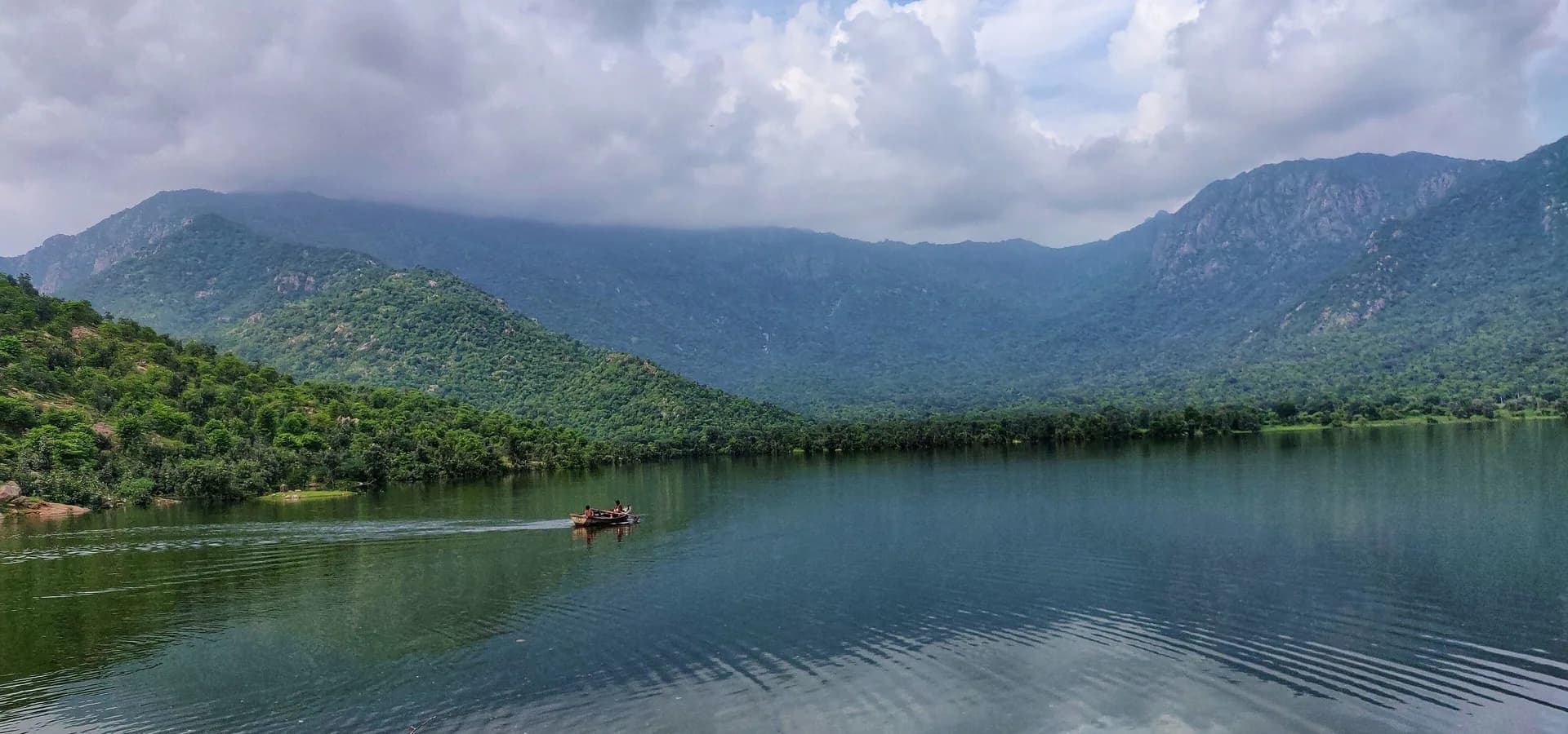 Still reservoir at Chandelao Dam near Abu Road, ringed by green Aravalli hills under heavy monsoon clouds