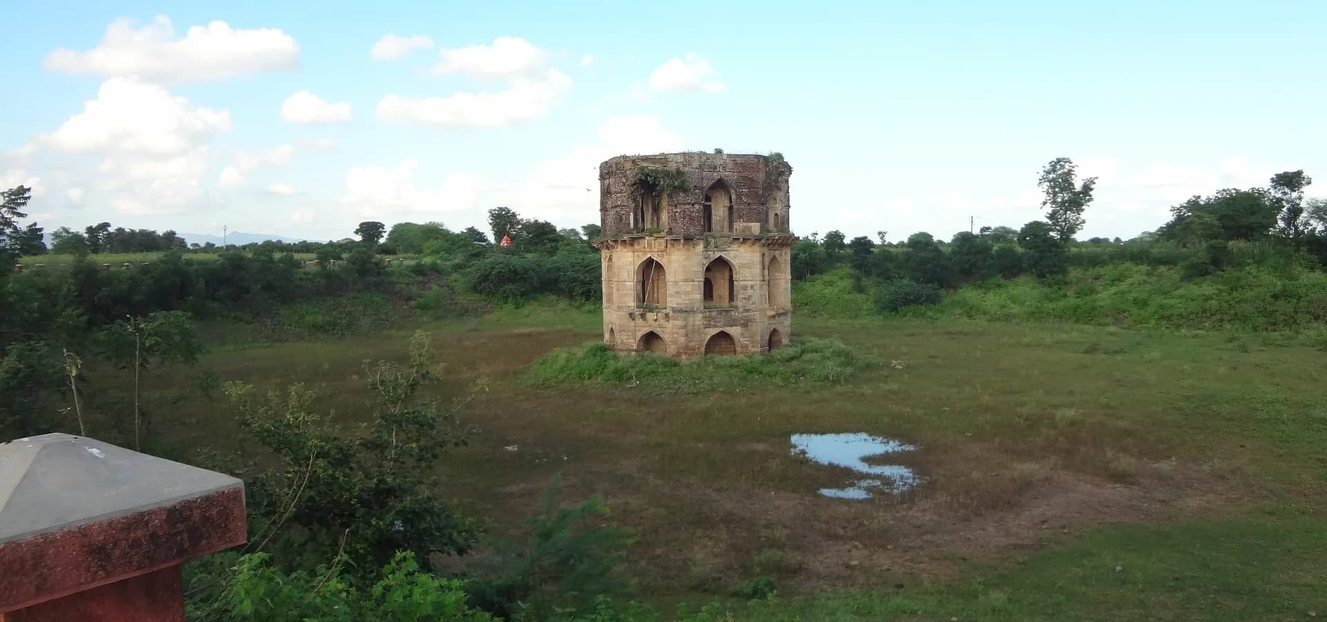 Der achteckige Steinpavillon von Hauz Katora erhebt sich aus einem grünen, grasigen Becken unter weitem blauem Himmel