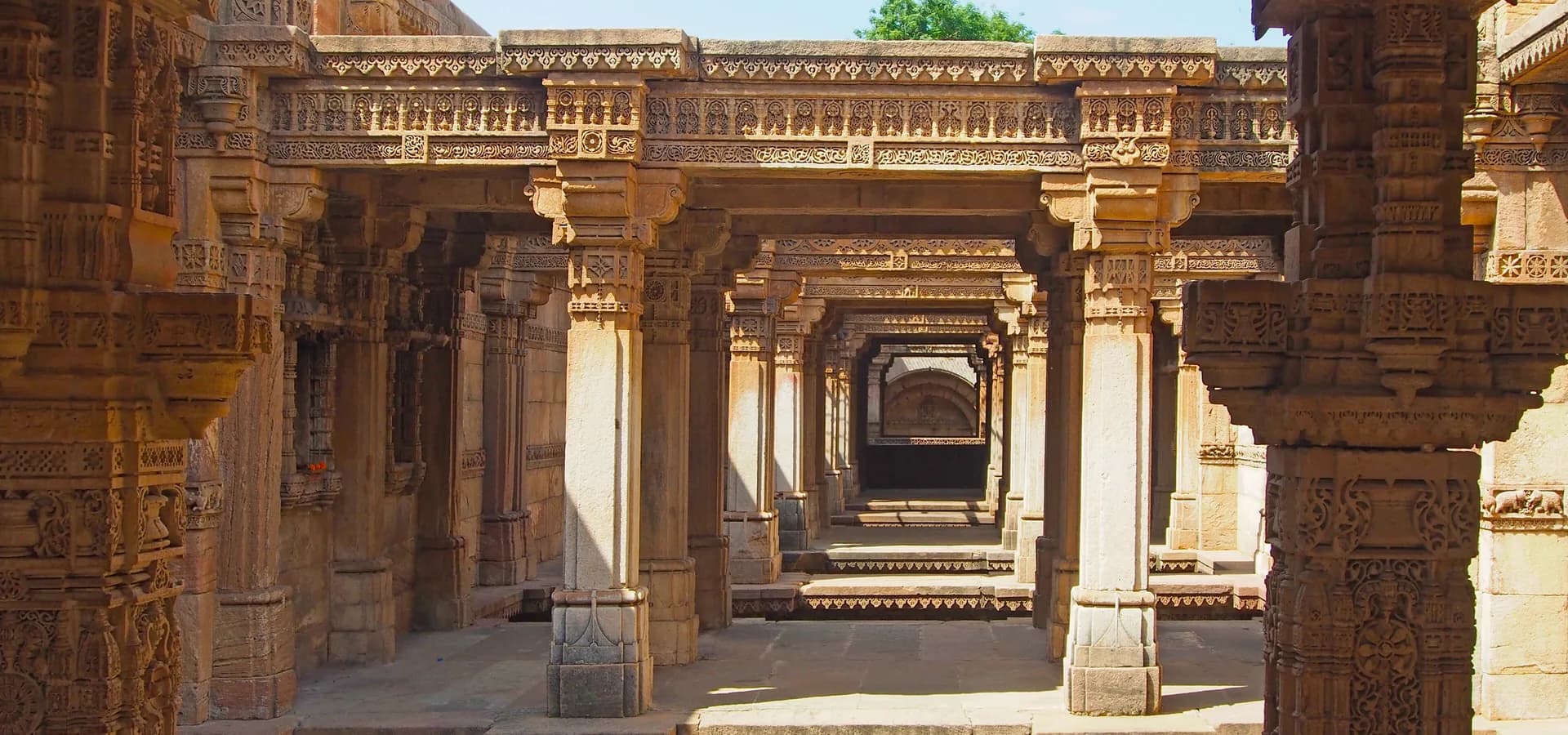 Fileiras de pilares e vigas de arenito entalhado se estendendo ao longe dentro do poço escalonado de Adalaj