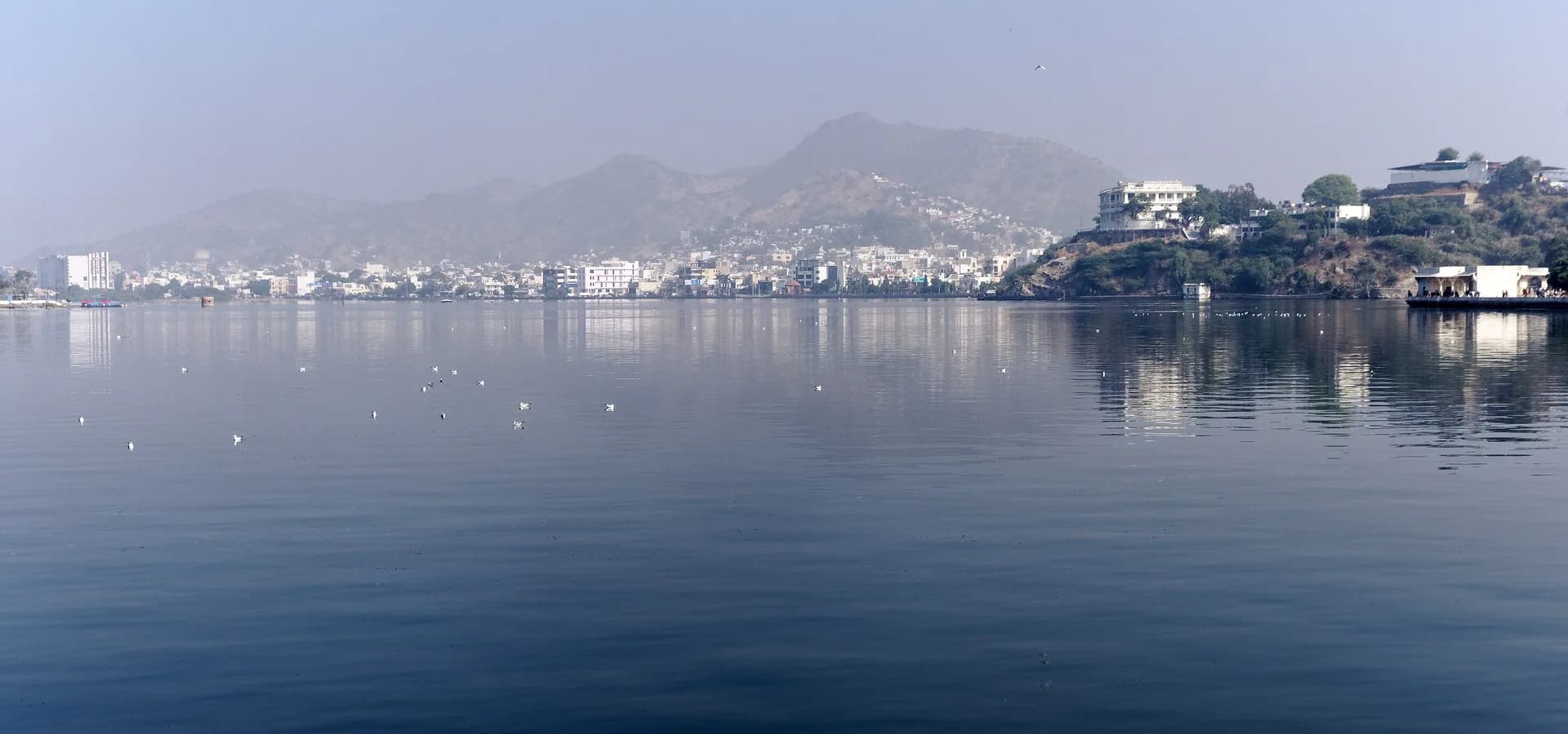 Aguas azules y tranquilas del lago Ana Sagar con casas blancas de Ajmer y las colinas Aravalli en la orilla lejana