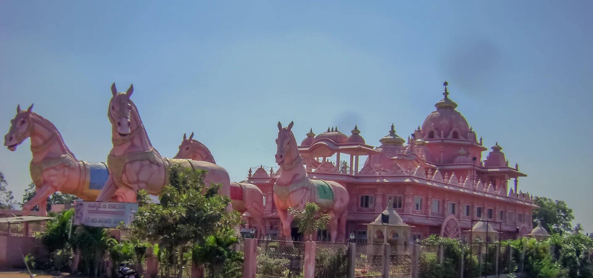 Estátuas rosa gigantes de cavalos diante do templo ISKCON em forma de carruagem, com cúpulas, perto de Anantapur