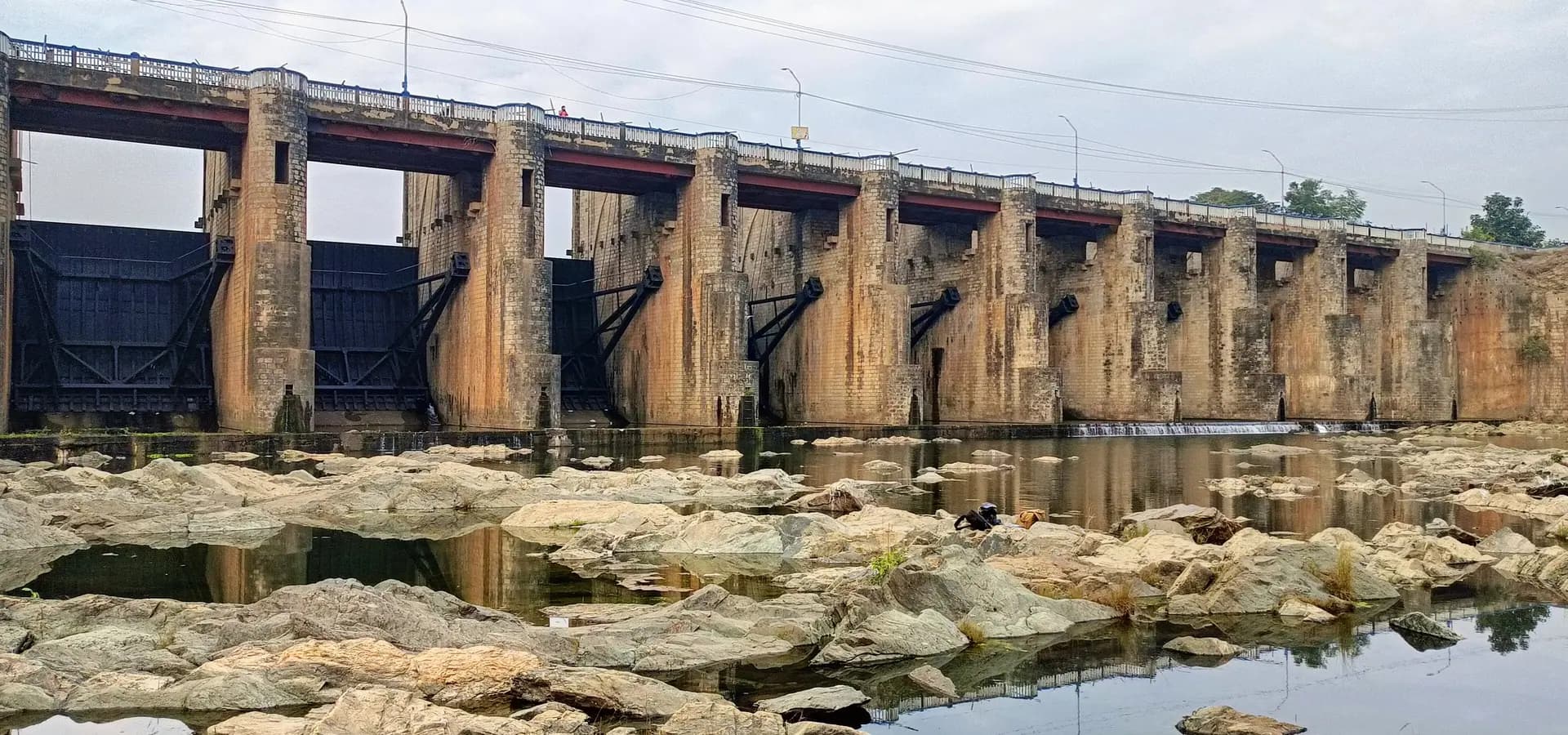 Stone spillway gates of Mukutmanipur Dam reflected in still water among pale river rocks