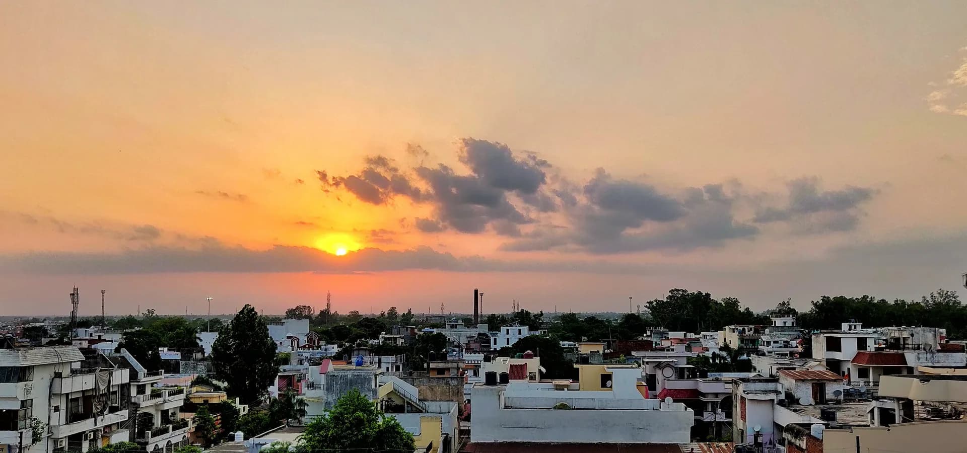 Oranger Sonnenuntergangshimmel mit verstreuten Wolken über flachen Dächern und Bäumen in Civil Lines in Bareilly