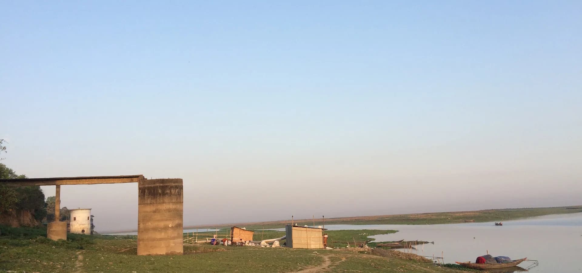 El ancho Ganges bajo un cielo despejado de primera hora en Bhagalpur, con un bote de madera amarrado junto a la orilla cubierta de hierba