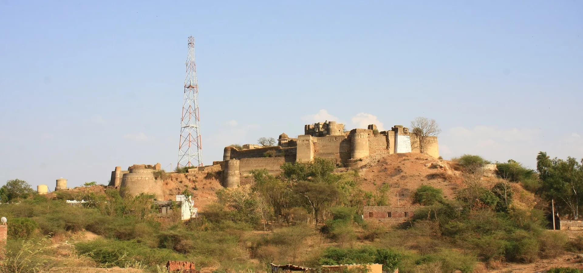 Alte Steinfestung mit runden Bastionen auf einem trockenen Hügel unter weitem blauem Himmel im Bezirk Bhilwara, Rajasthan