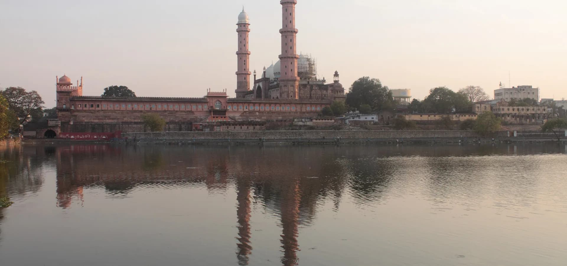 O Taj-ul-Masajid, com seus dois altos minaretes refletidos em um lago calmo sob um suave céu rosado de fim de tarde