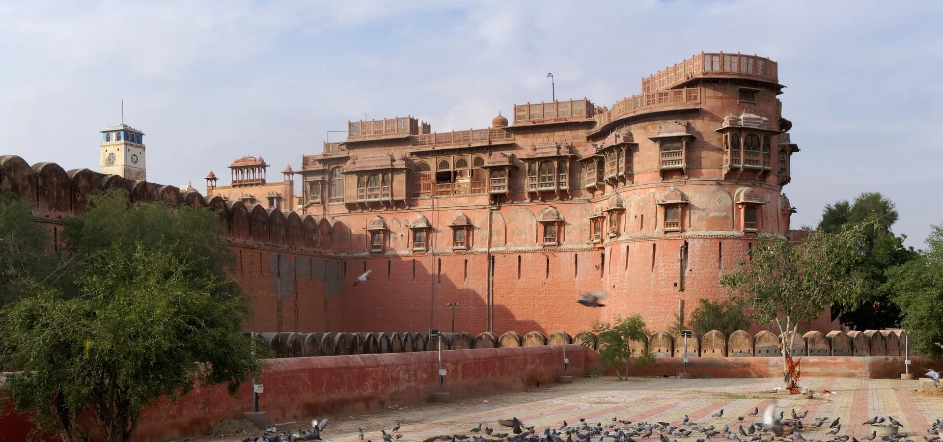 Muralhas de arenito vermelho e palácios com sacadas do Forte de Junagarh sob um céu pálido, com pombos no pátio