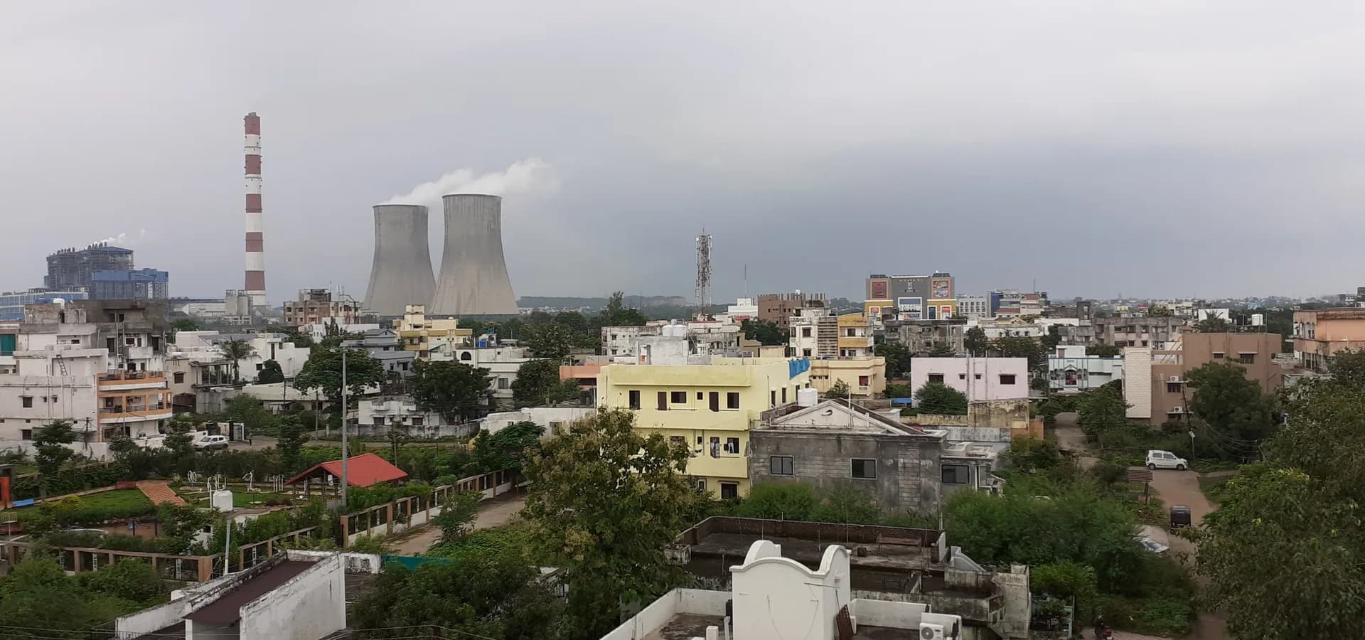 Wide view over Chandrapur's rooftops and trees, power station cooling towers and a chimney under a cloudy sky