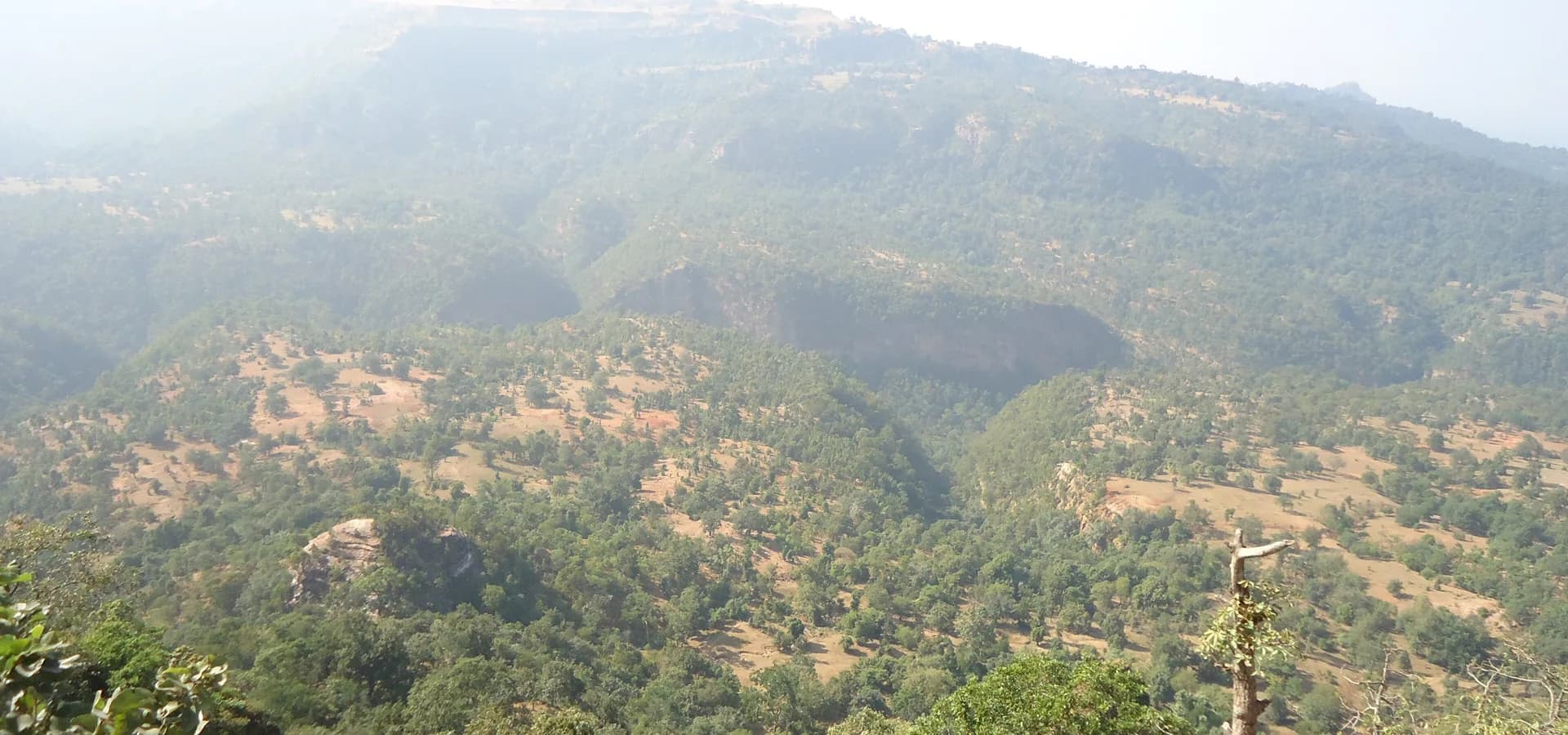 Bewaldete Hänge und felsige Klippen des Patalkot-Tals in den Satpura-Hügeln unter dunstigem Himmel